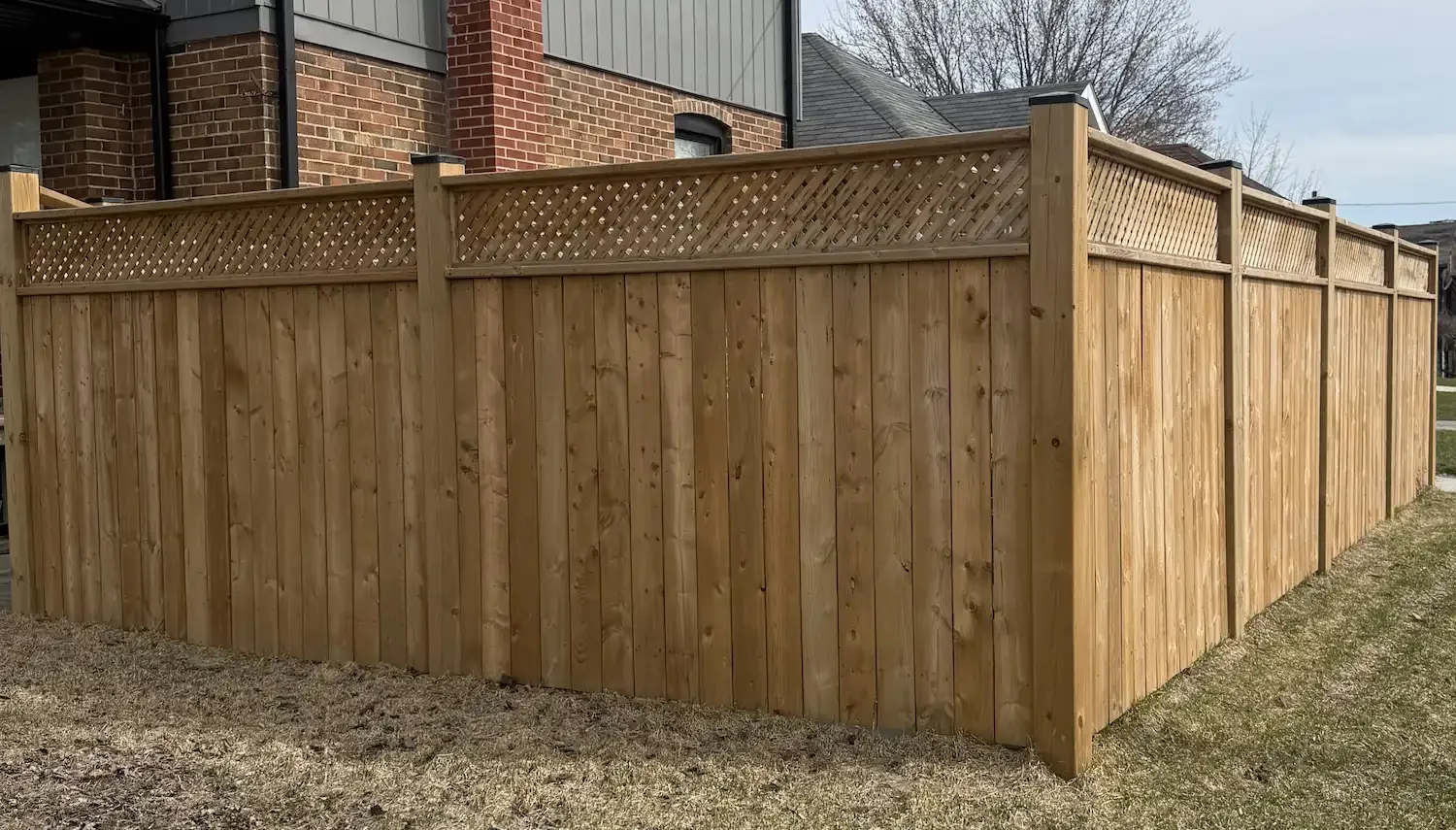 Wooden privacy fence surrounding a residential backyard with a brick house in the background.