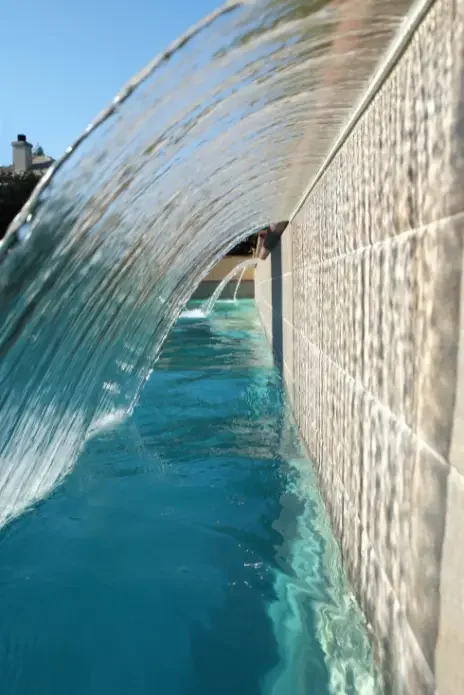 Close-up view of a water feature with a curved glass or acrylic barrier, showing water flowing over it into a pool.