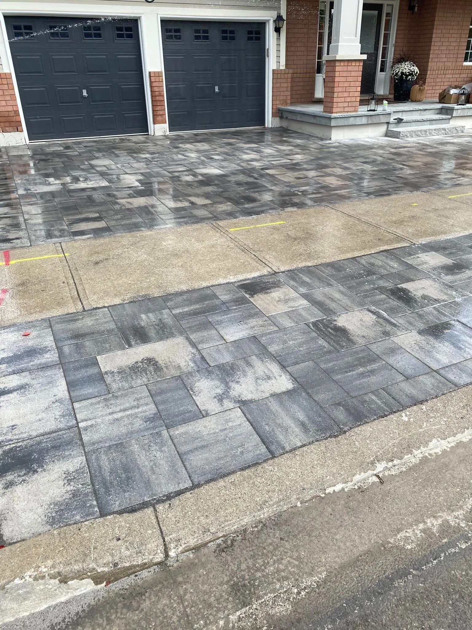 Wet, modern driveway with textured gray paving stones in front of a garage.