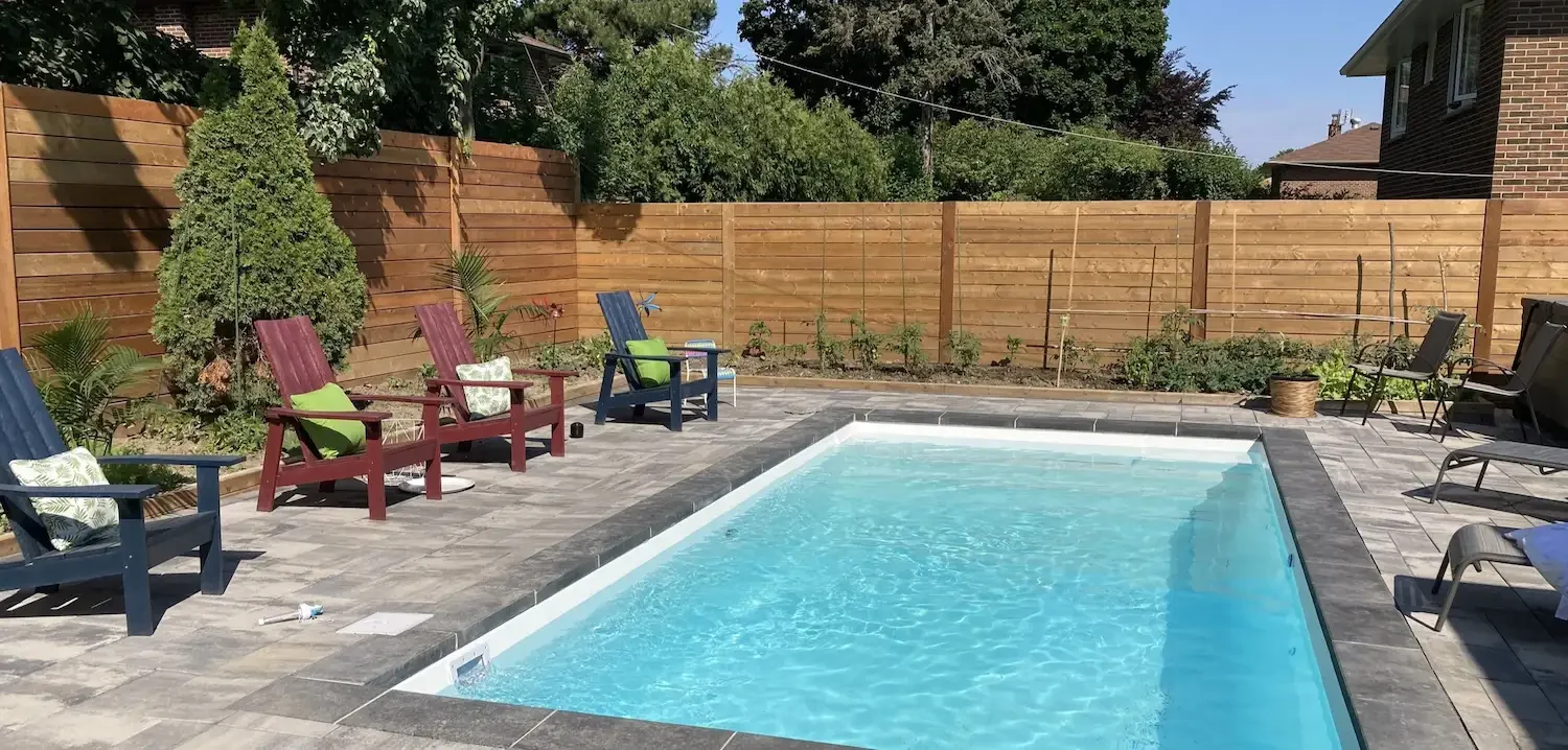 Backyard with a swimming pool, wooden fence, outdoor chairs, and plants.