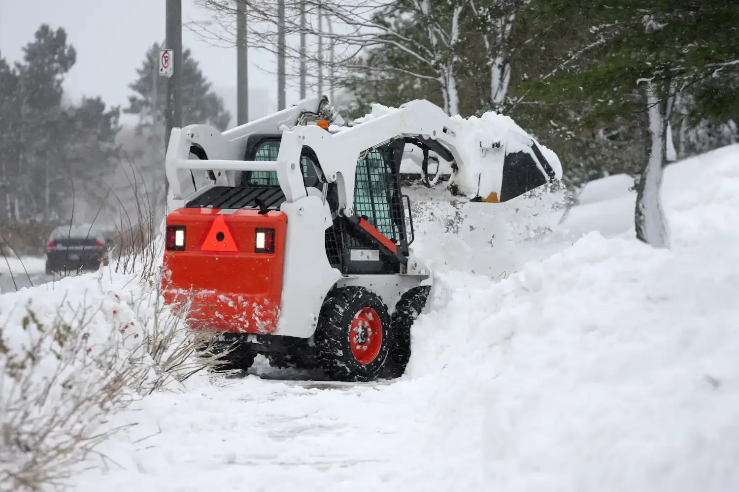 A skid-steer loader with a snowplow blade clearing snow from a road.