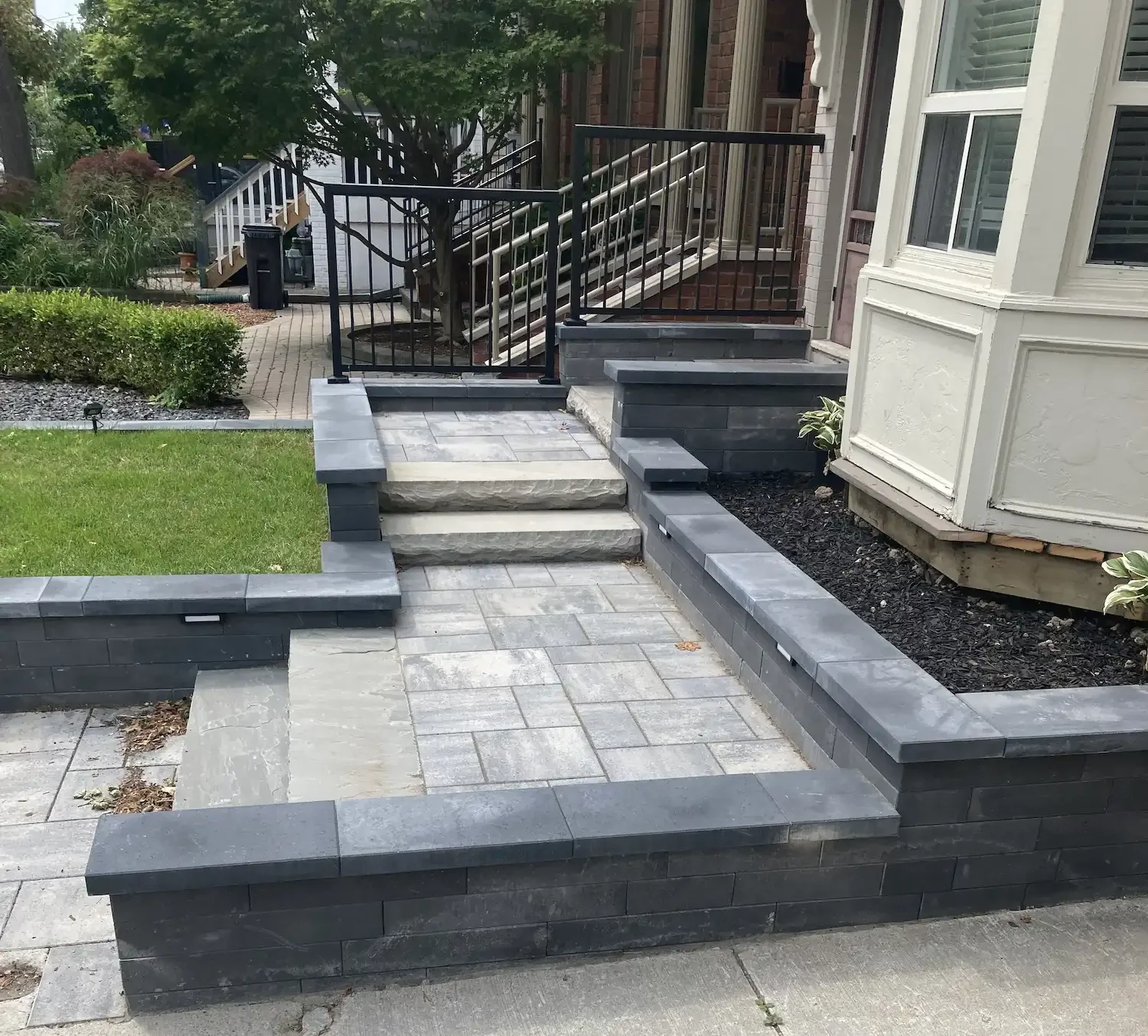 Front yard with stone and brick steps, black metal railing, and landscaped garden area.