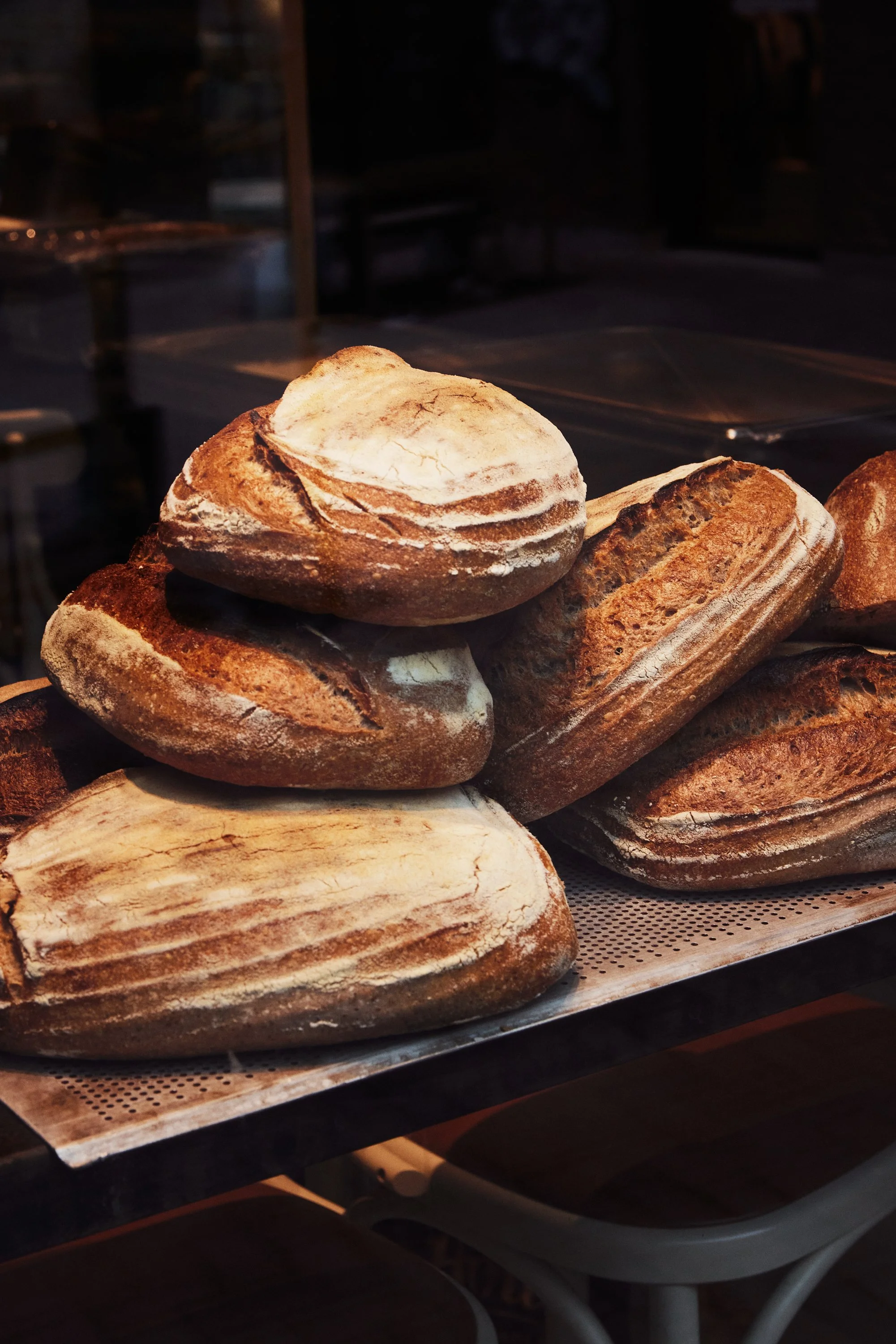 Ulike typer brød som er utstilt på en bakeri- eller kafédisk, inkludert runde, avlange og baguettlignende brød med sprø skorpe.