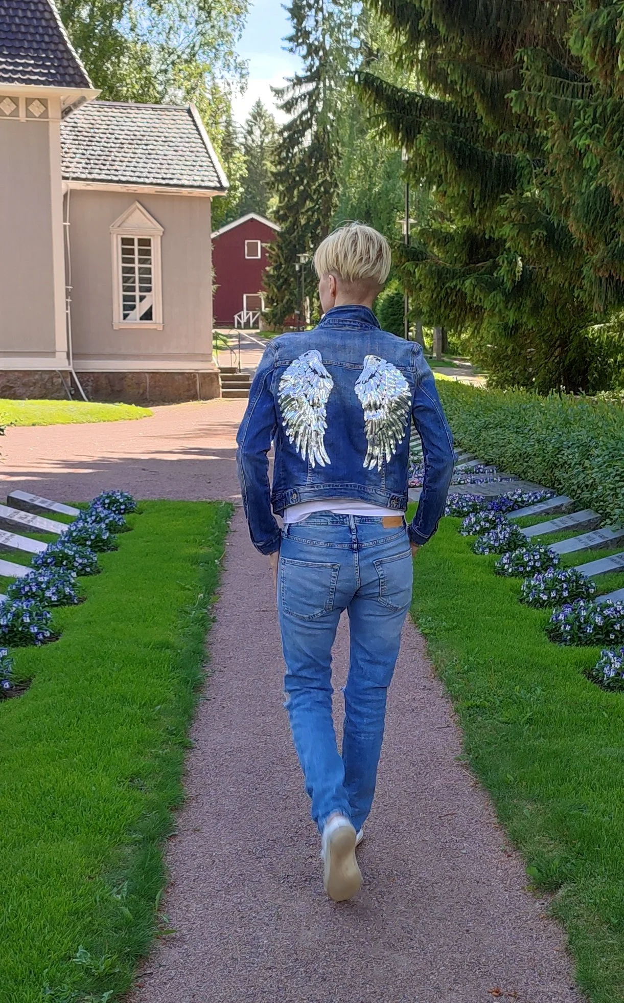 Person walking on path wearing denim outfit with angel wings on jacket