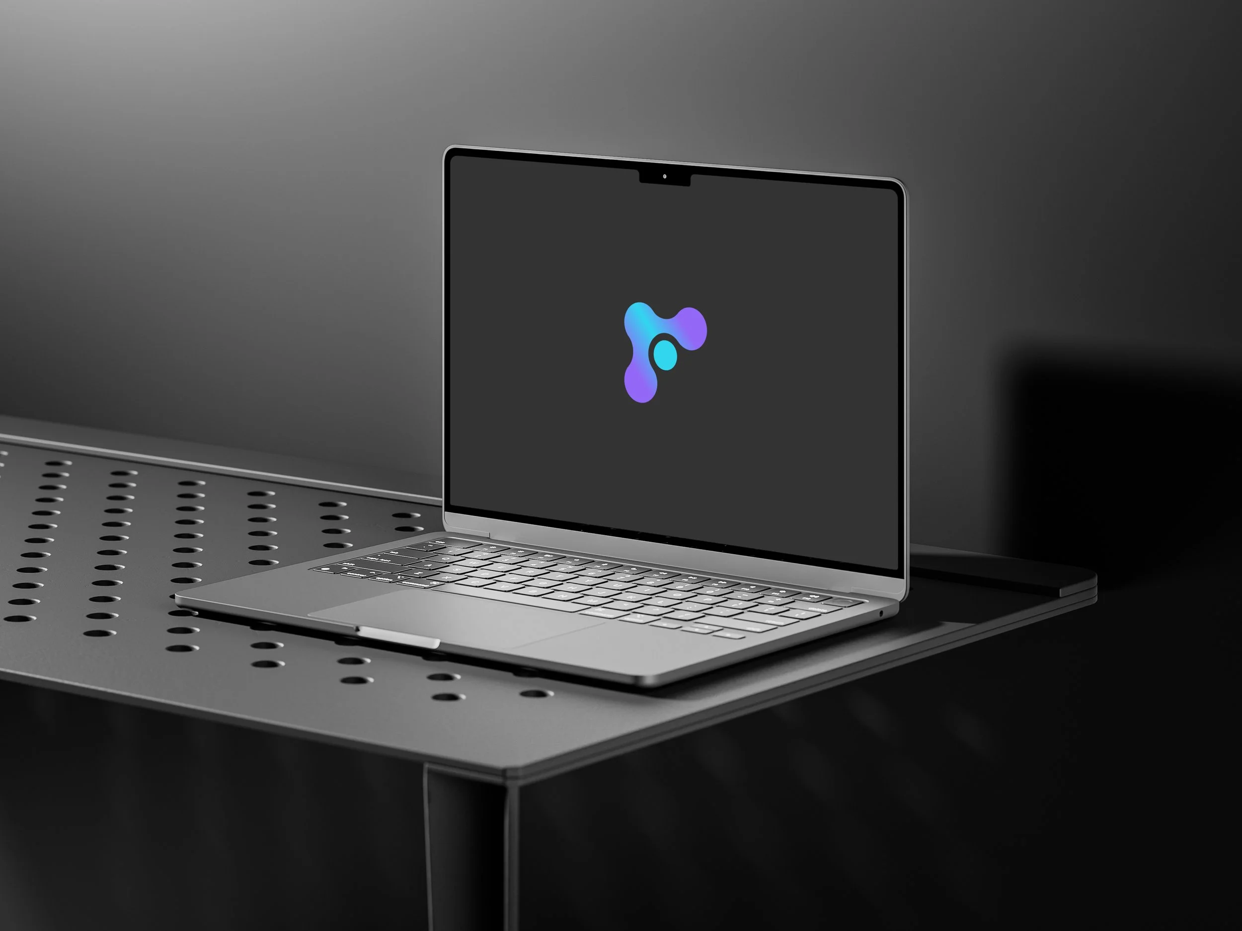 A laptop with a dark screen displaying a colorful logo, sitting on a perforated metal surface against a plain gray background.
