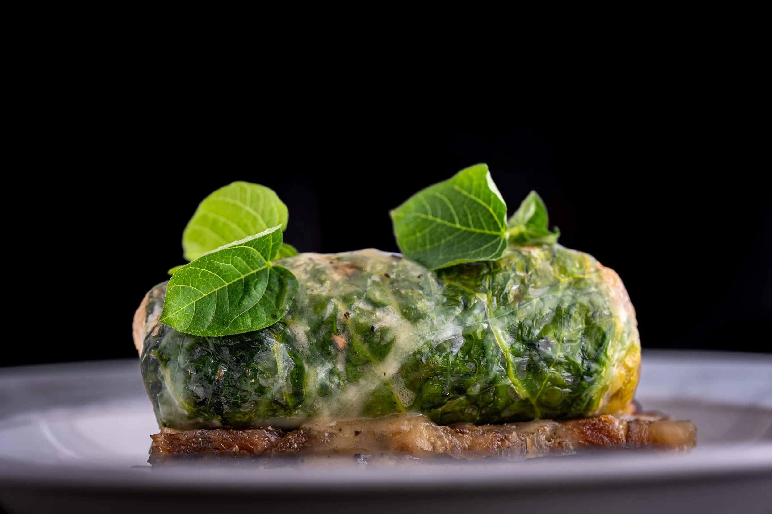 Plat de pâté en croûte recouvert de feuilles de chou vert et de feuilles de basilic, présenté sur une assiette blanche avec un fond noir.