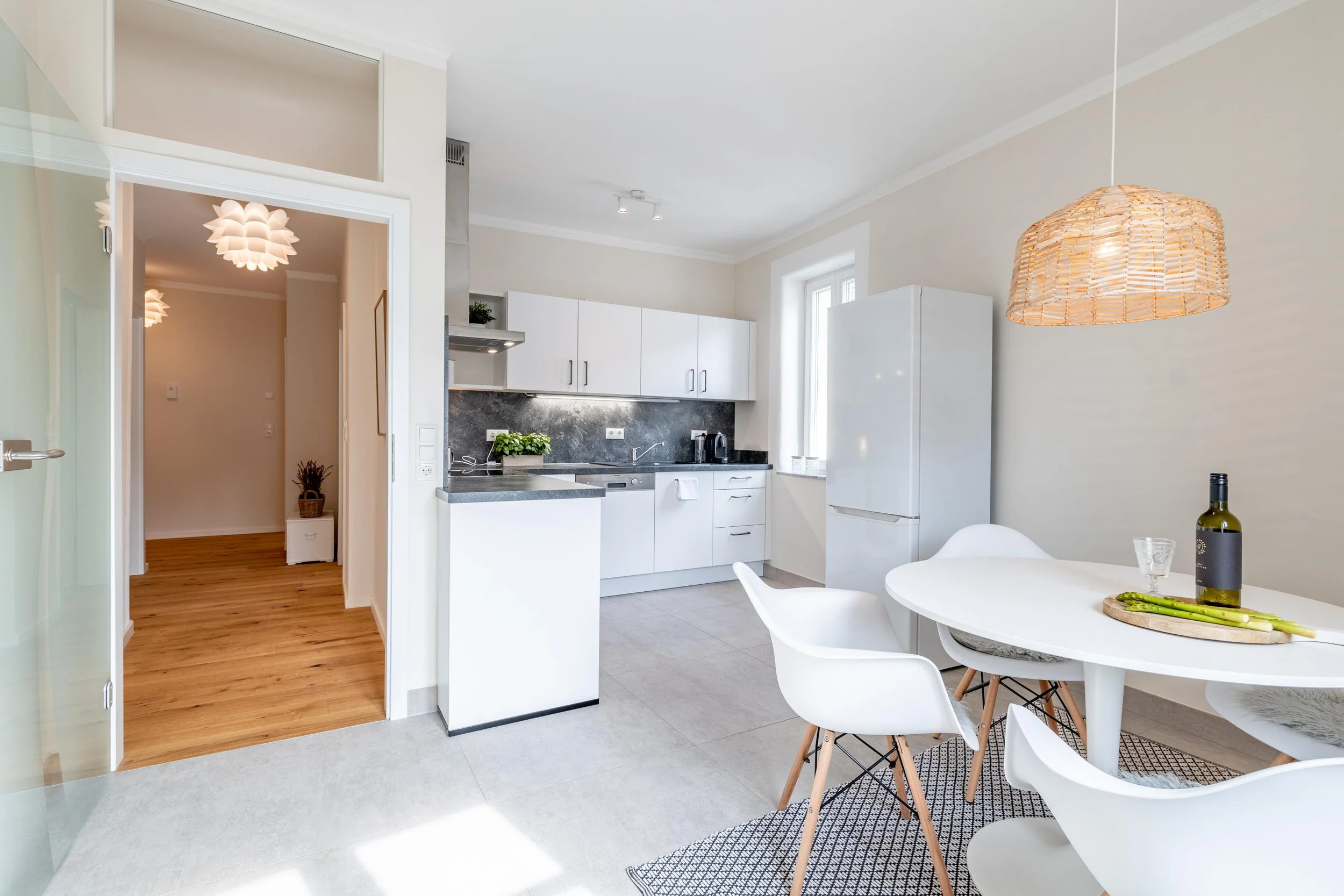 Cuisine moderne avec table ronde blanche, chaises blanches, luminaires en rotin, frigo blanc, et décoration minimaliste.