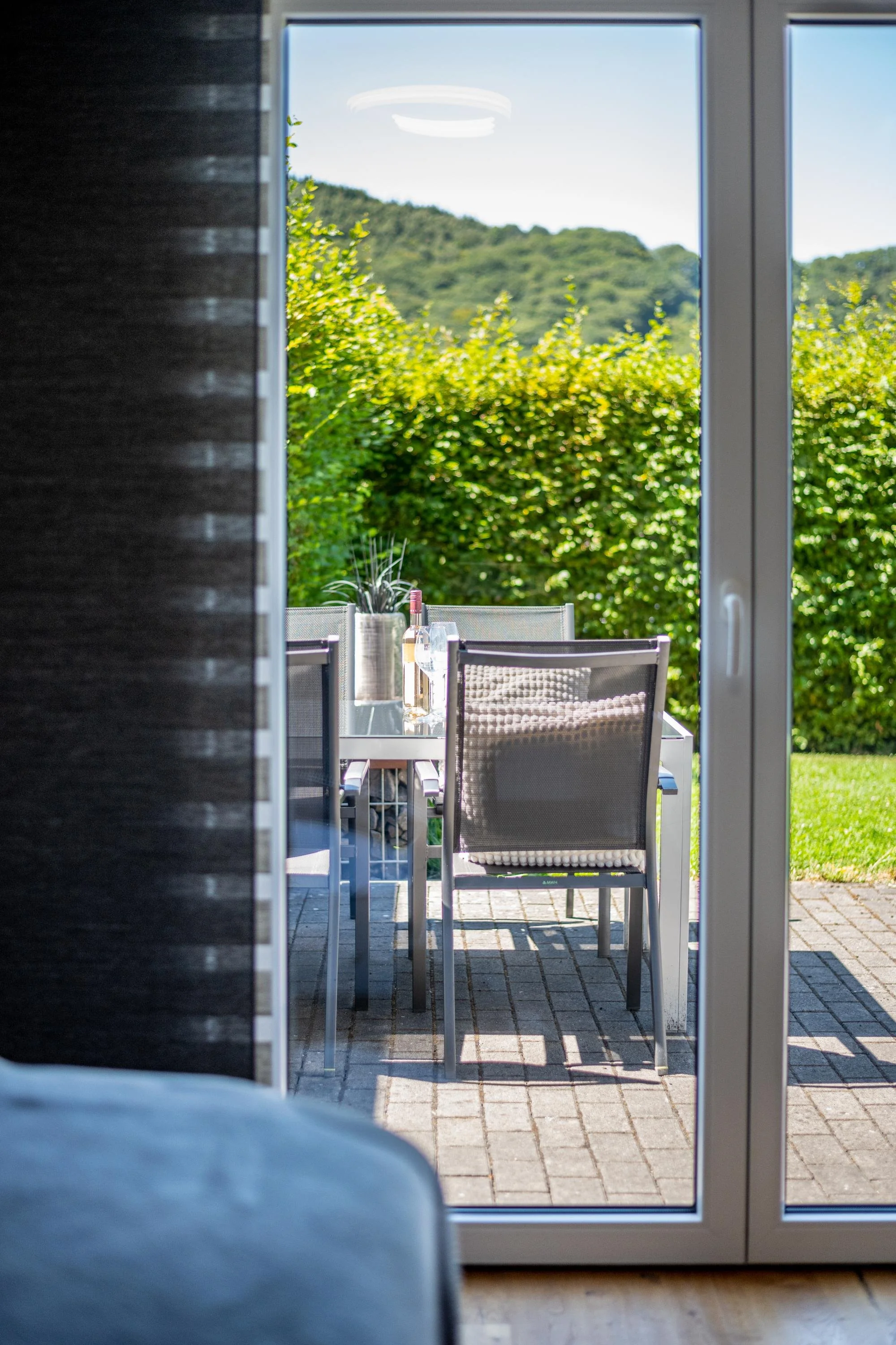 Vue d'une terrasse avec une table et des chaises, vue à travers une porte-fenêtre avec un paysage de verdure et de collines en arrière-plan.