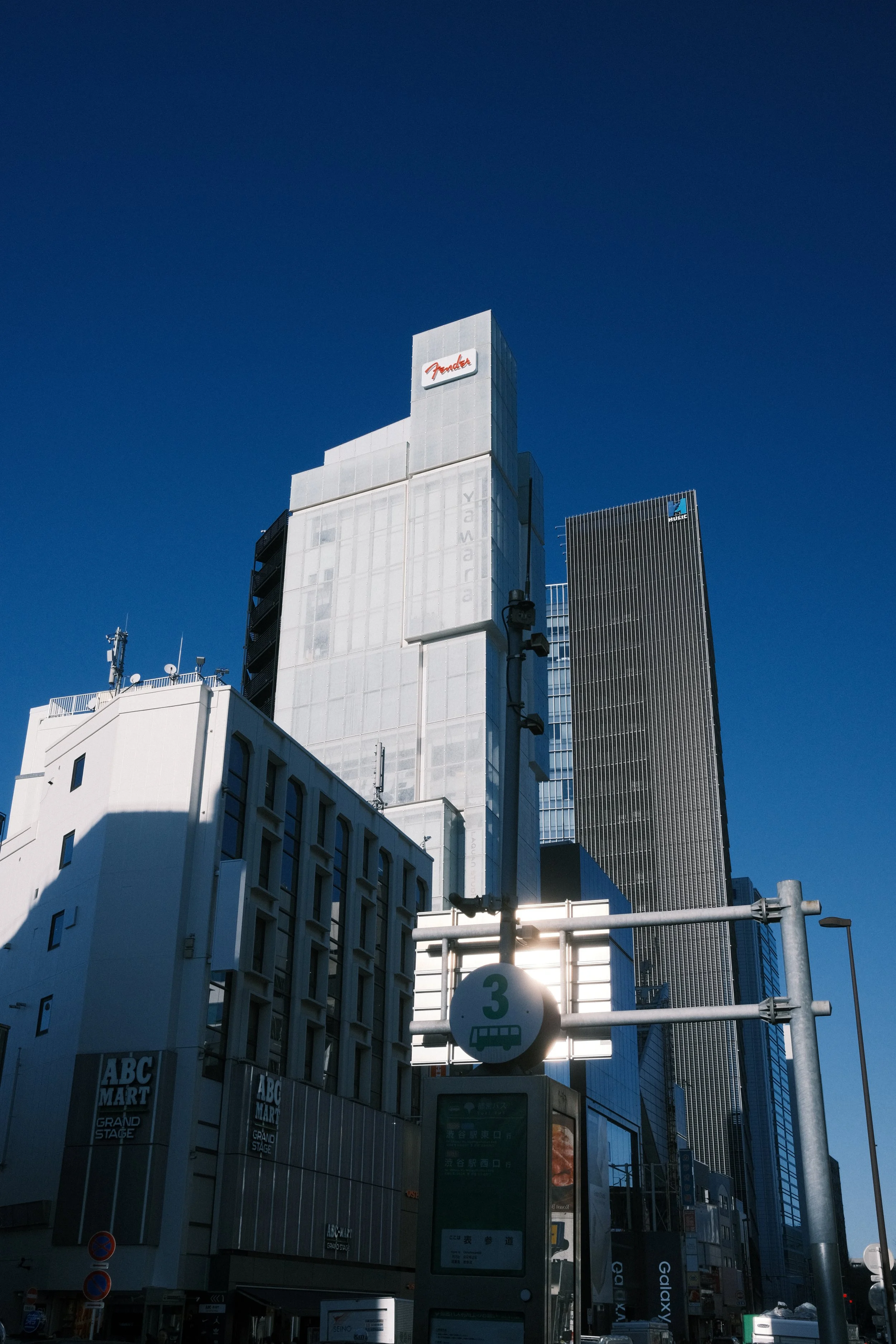 Tall buildings in a city with a blue sky, featuring signs for ABC Mart and other businesses.