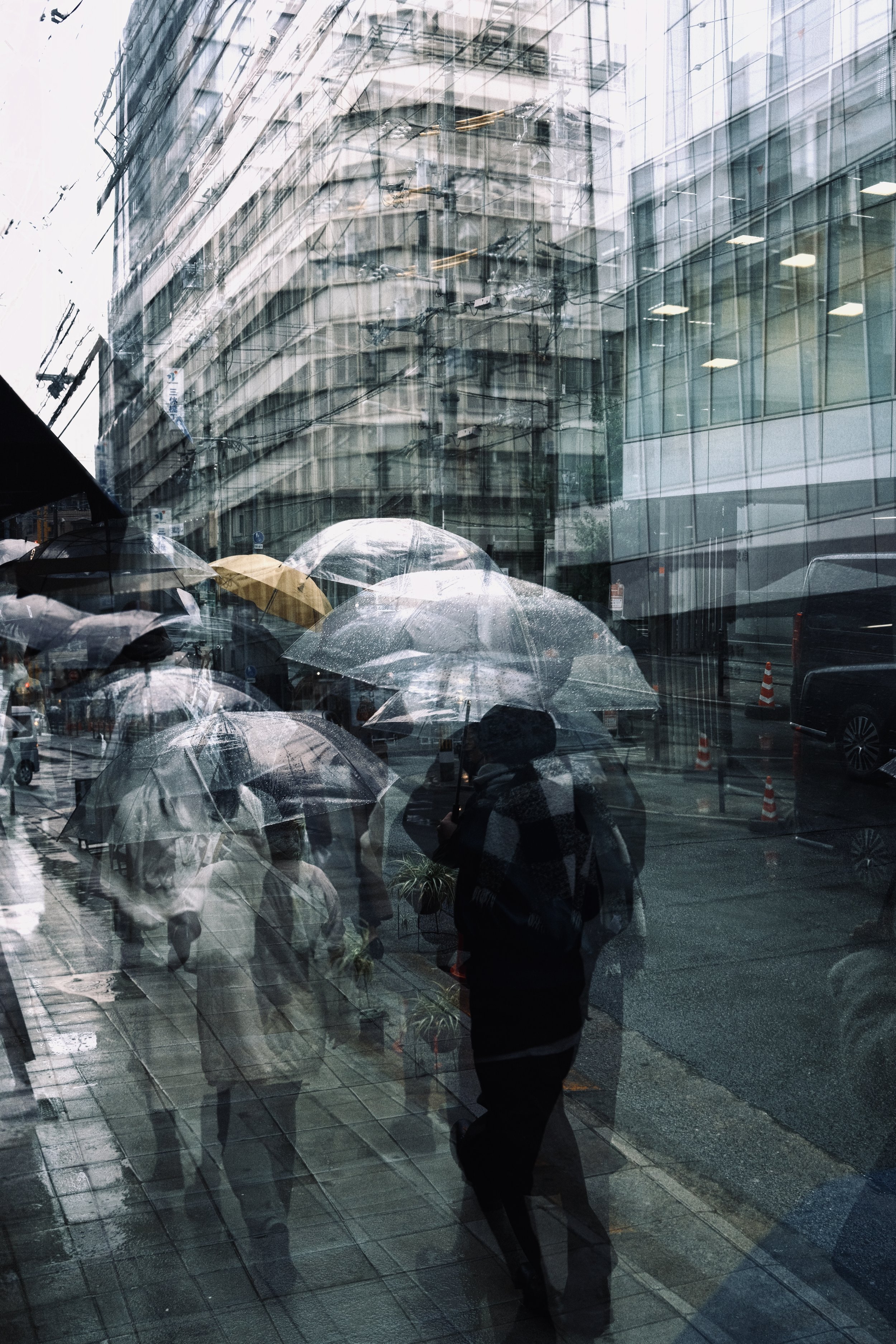 People walking with umbrellas on a rainy day, captured through a glass window with reflections of buildings and cityscape.