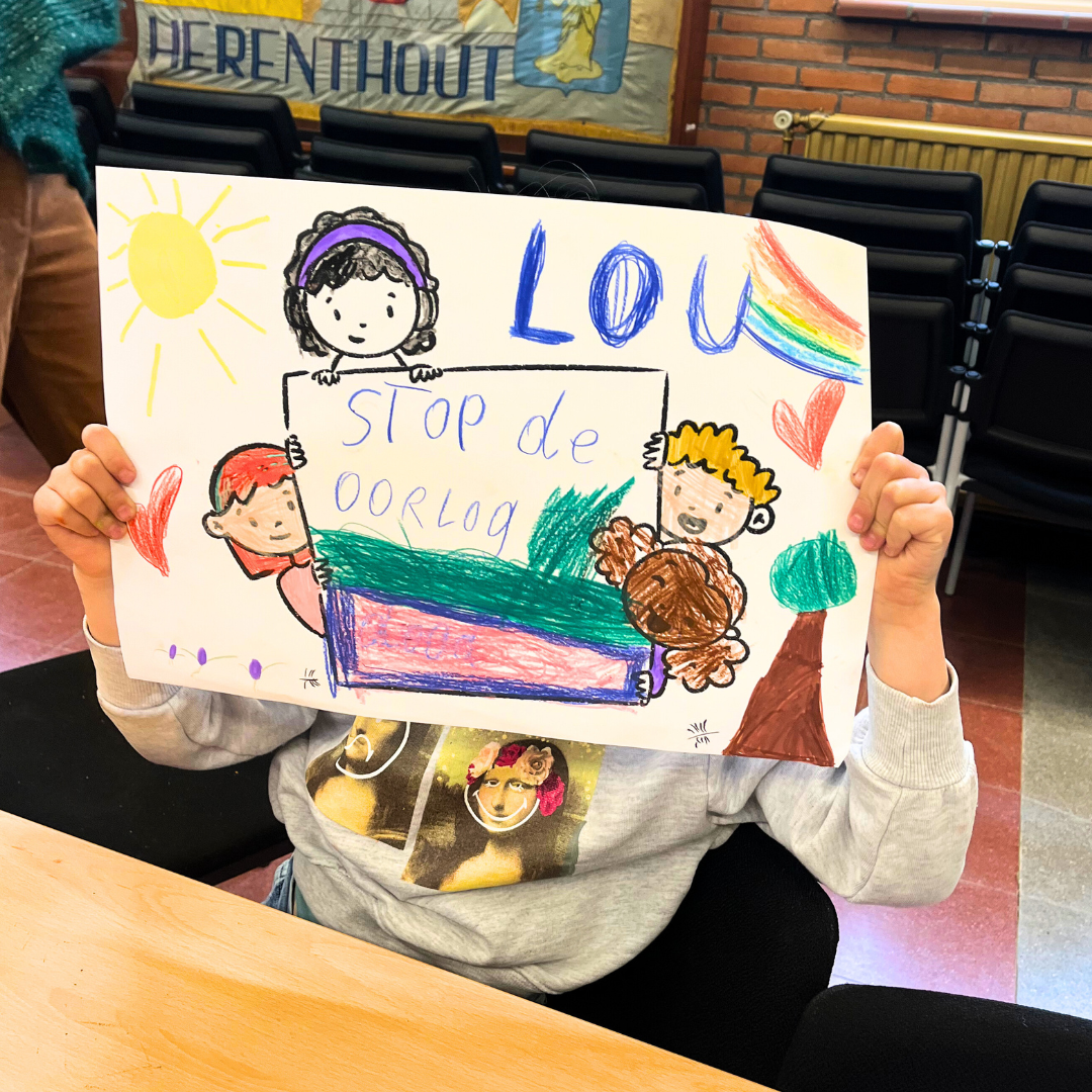 Kind houdt tekening vast met regenboog, zon, bomen, hart en kinderen, met tekst 'Stop de oorlog' en 'Louw' erop.