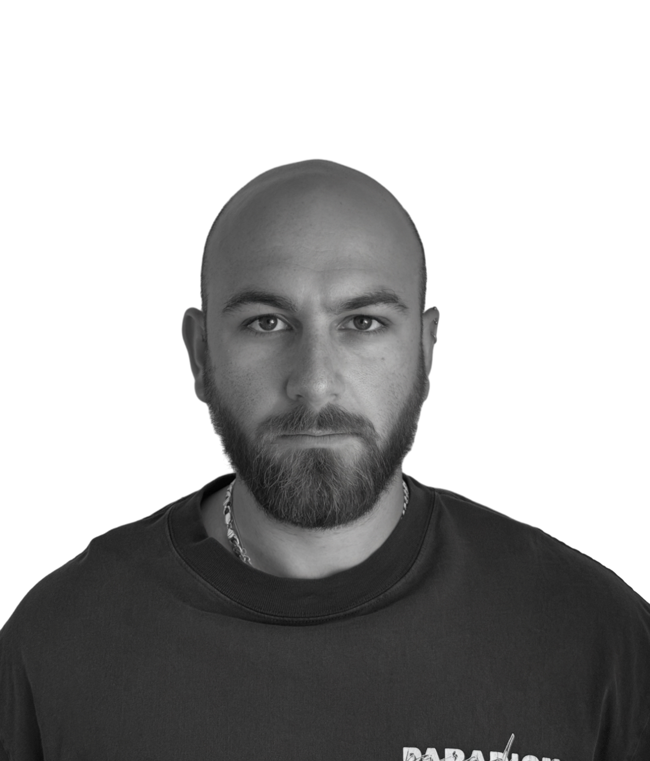 Black and white portrait of a bald man with a beard, wearing a dark t-shirt and a chain necklace, looking directly at the camera.