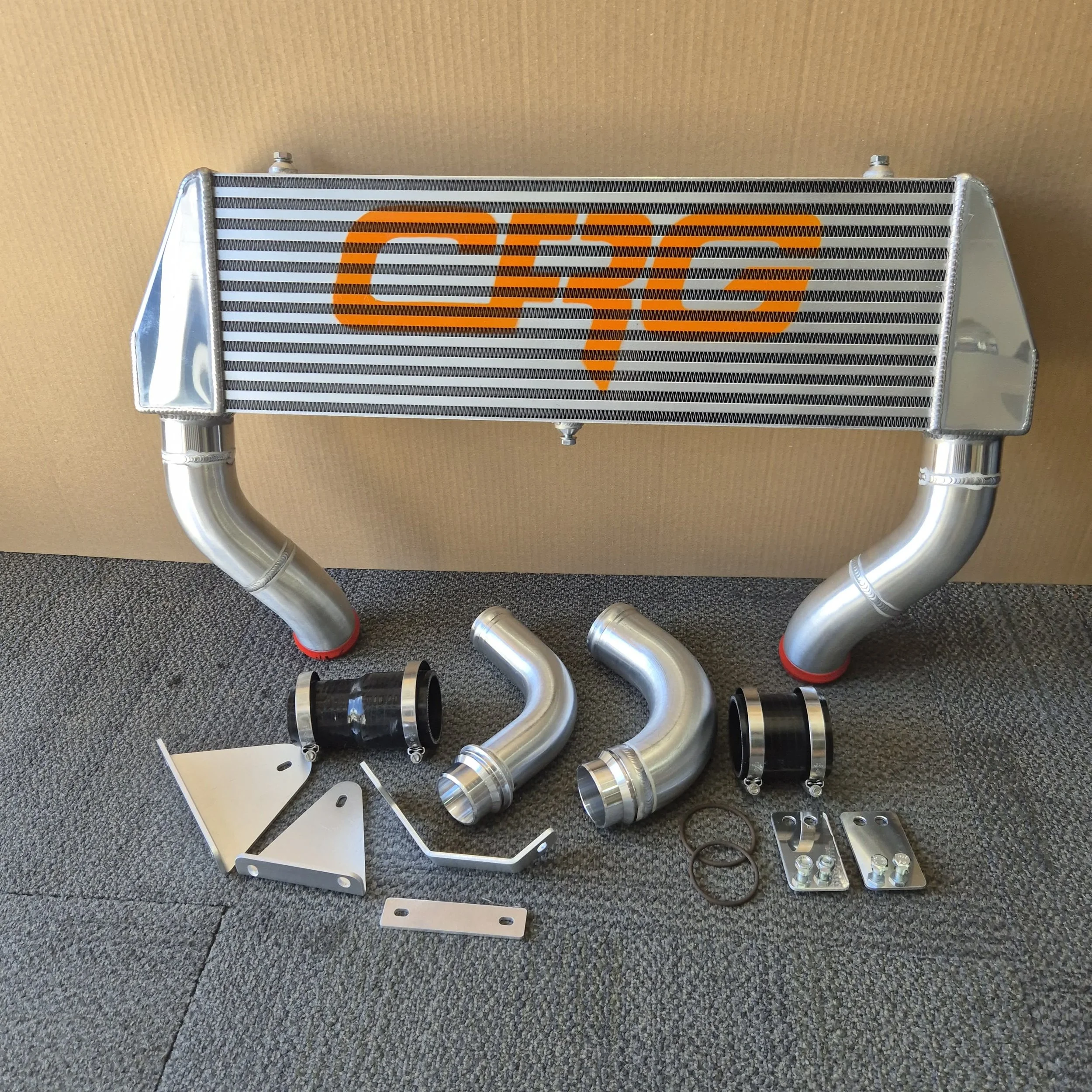 An automotive intercooler with orange GSG logo, metal pipes, clamps, and mounting hardware