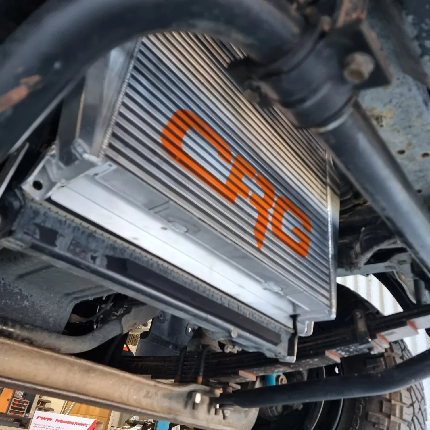 Close-up view of a car radiator with the logo 'QHYG' in orange on it, located under the vehicle's chassis.