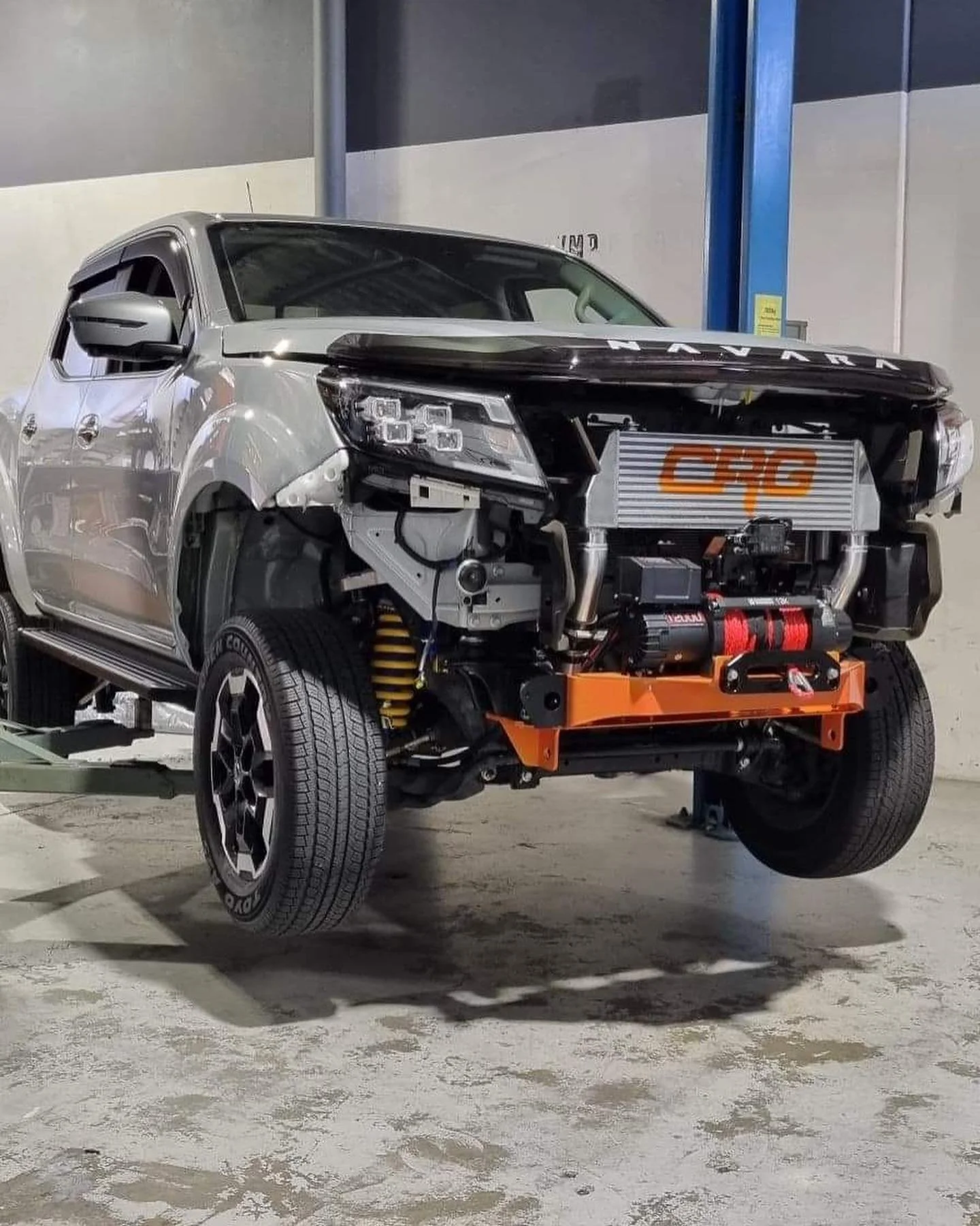 Partially assembled Silver Land Rover vehicle on a lift with front end disassembled, exposing internal components and orange frame