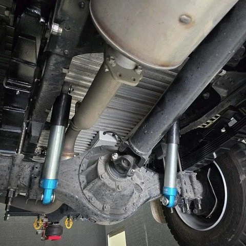 Underneath view of a vehicle's rear differential, with shock absorbers and suspension components visible.