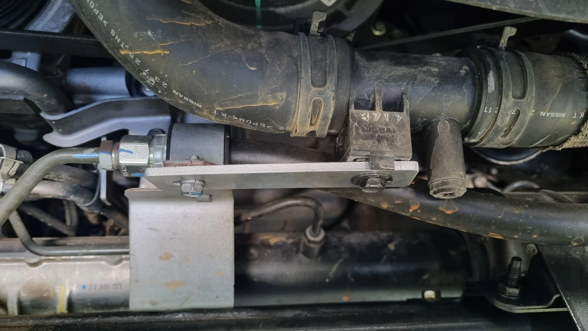 Close-up of a vehicle's engine component, showing hoses, metal fittings