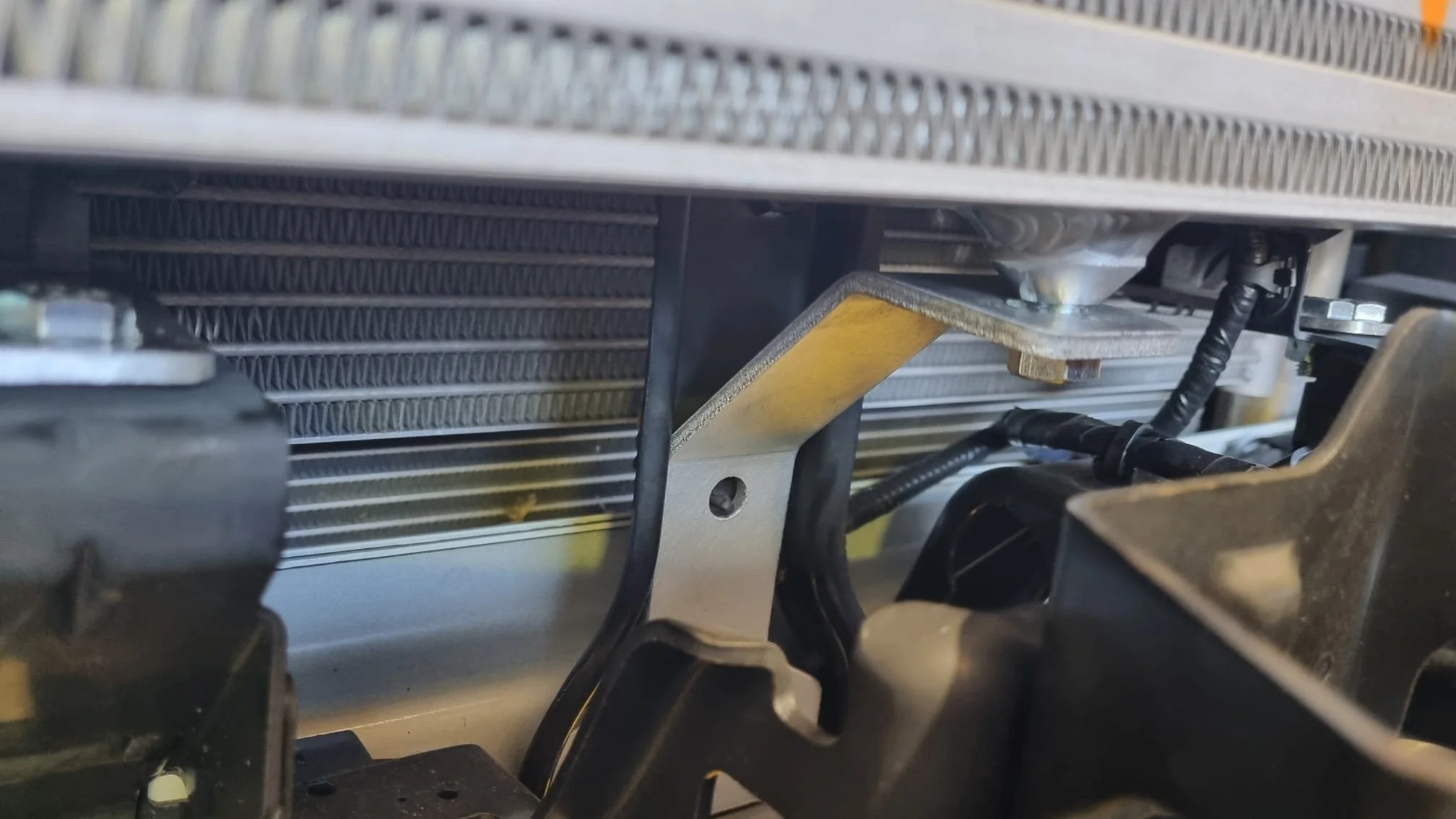 Close-up of a metallic structure with black cables, a black plastic component, and a metallic plate attached to a radiator or cooling system.