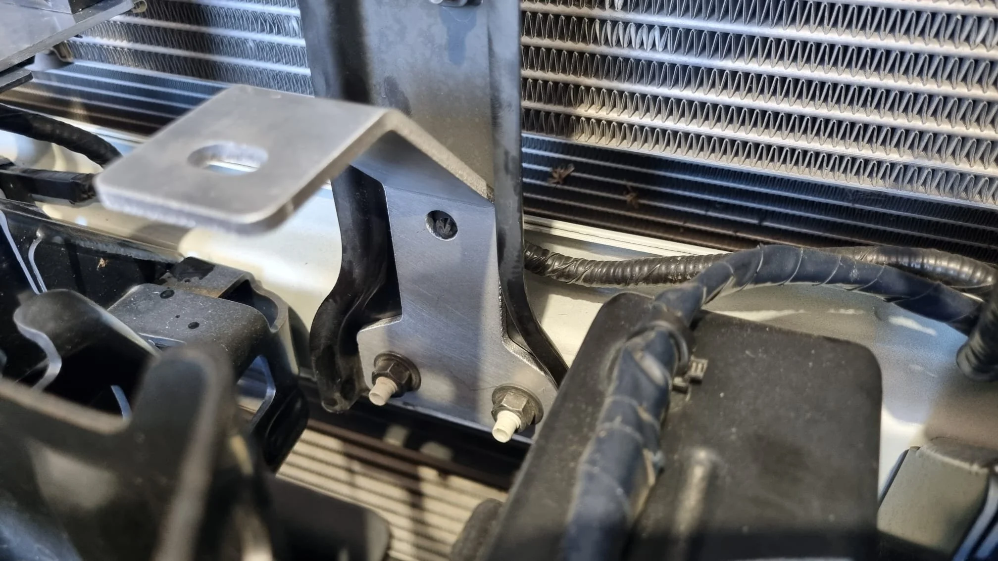 Close-up of a car radiator and related components, including mounting brackets, bolts, and electrical wiring.