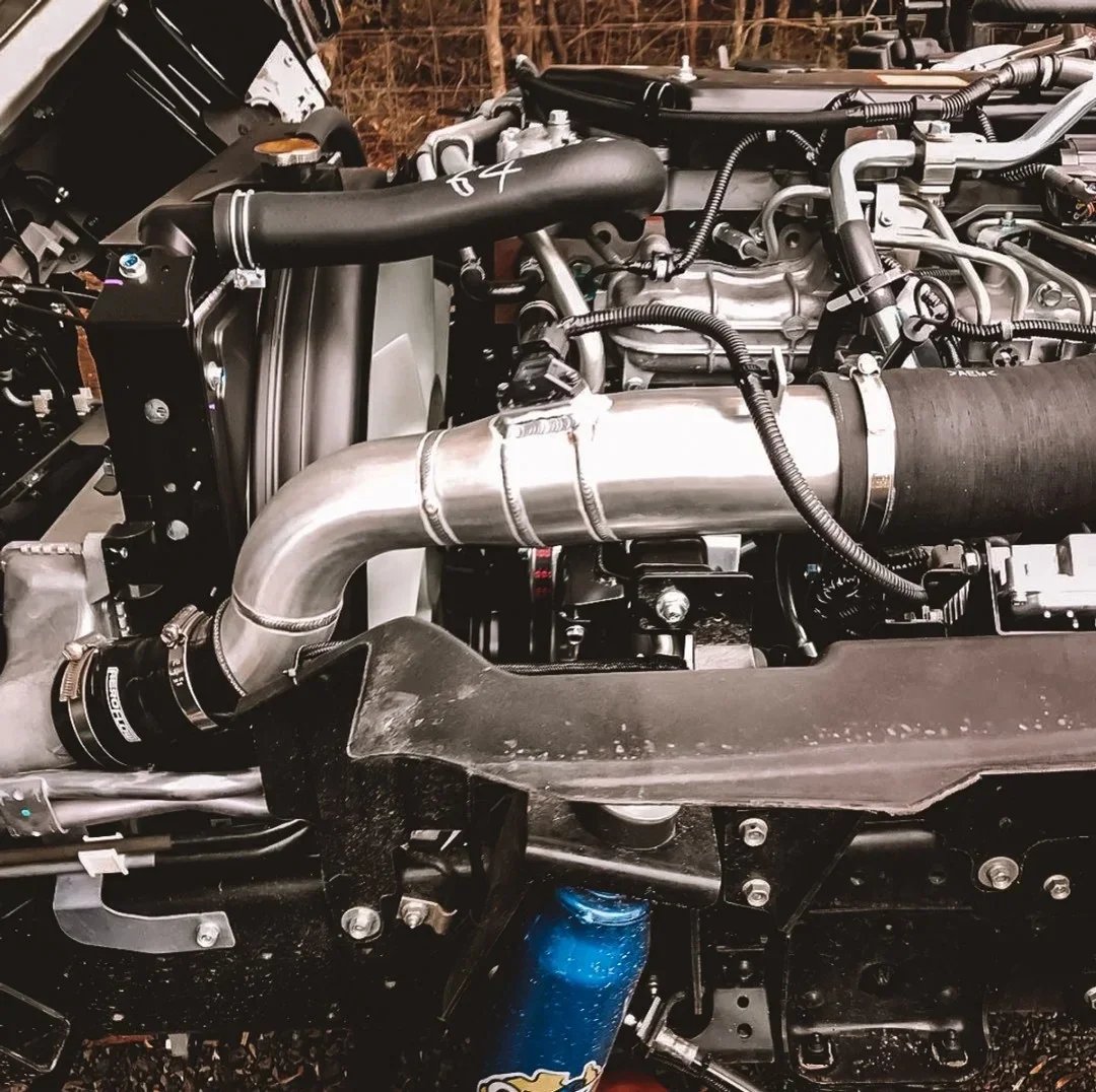 Close-up of a car engine with visible pipes, hoses, and mechanical components.