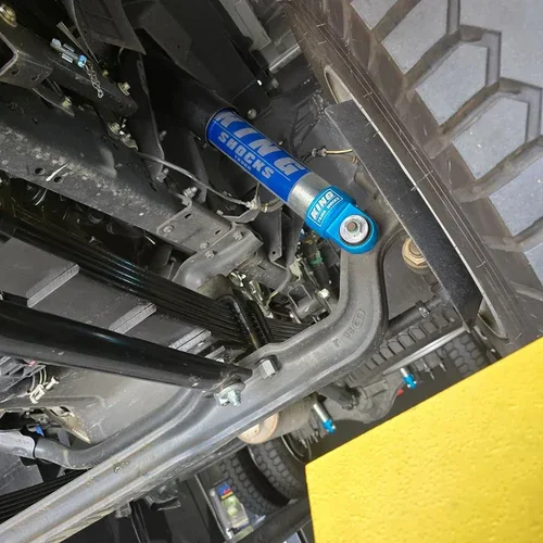 Close-up of vehicle suspension system showing a blue shock absorber with the brand name 'FOX' and other mechanical parts.