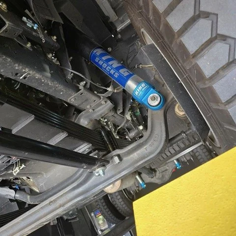Close-up of a vehicle's suspension and steering components, including a blue Shock Tech shock absorber