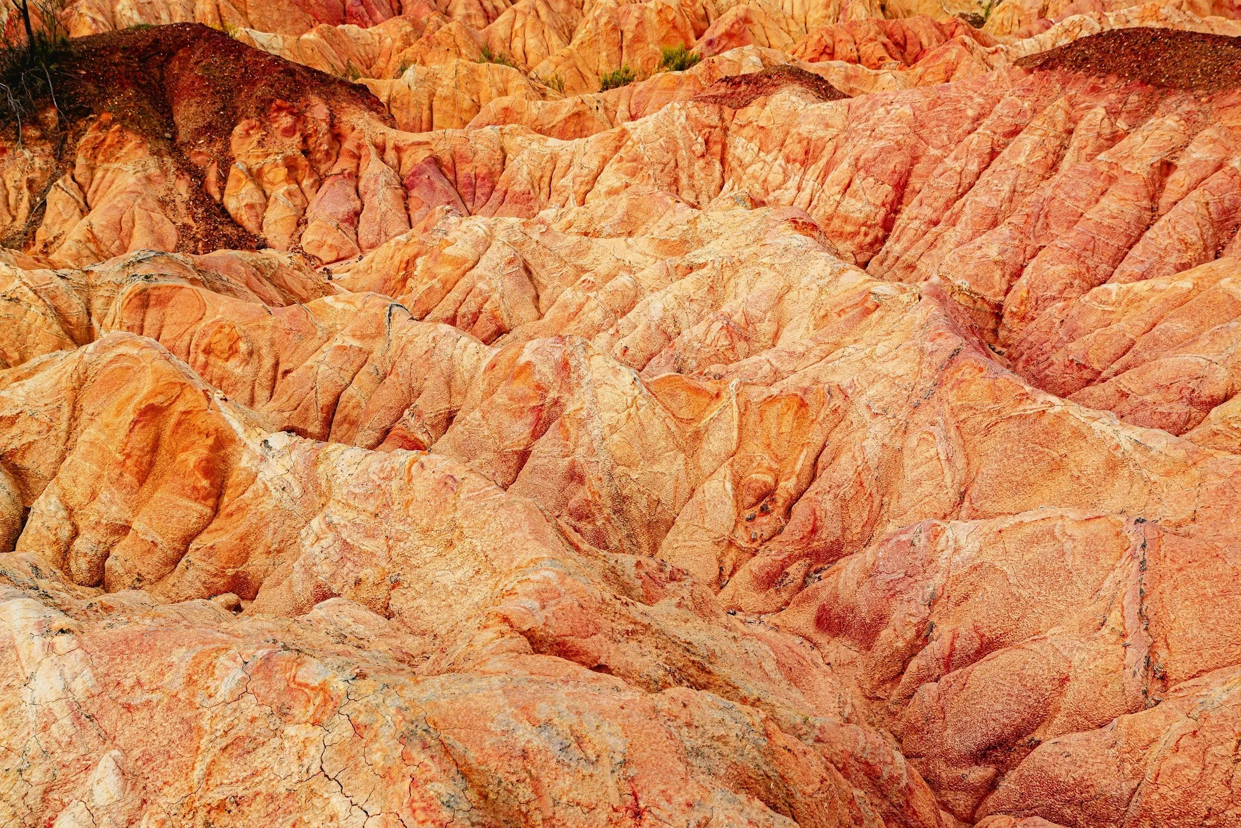 Colorful layered rocks in red, orange, pink, and white hues with some dark patches and cracks.
