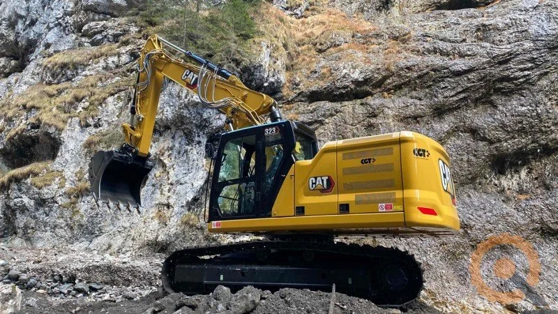 Escavatore giallo CAT 323 su un terreno roccioso in montagna.