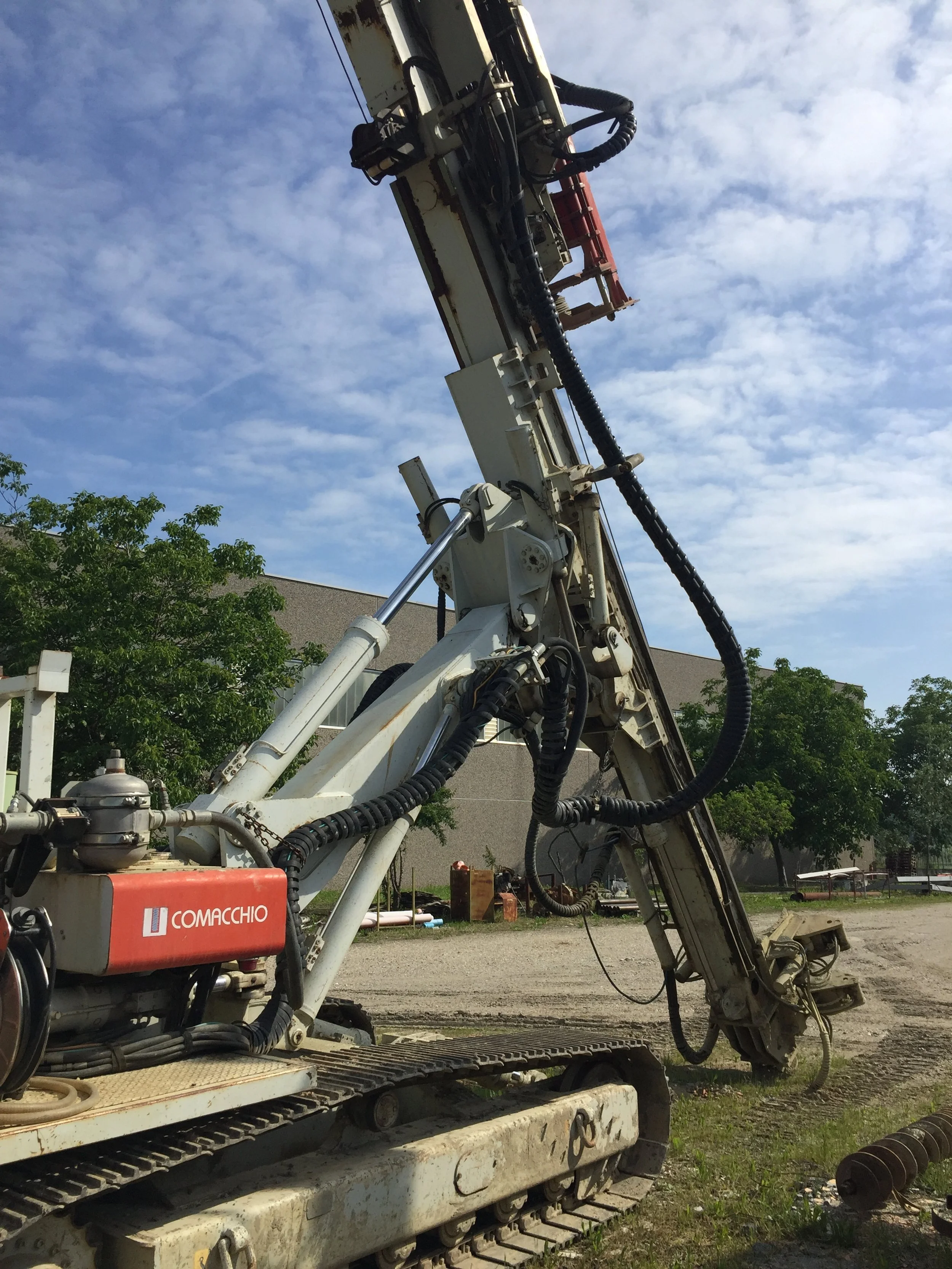 Macchinario perforatore Comacchio su un sito di costruzione con cielo azzurro e alberi sullo sfondo.