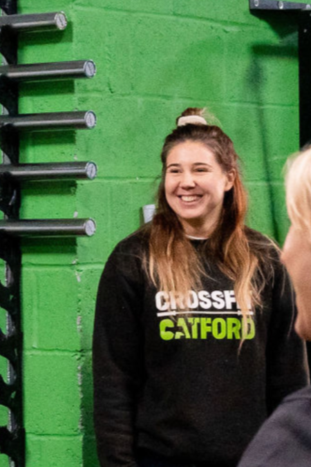 Person smiling with long hair, wearing a black sweatshirt, against a dark background.
