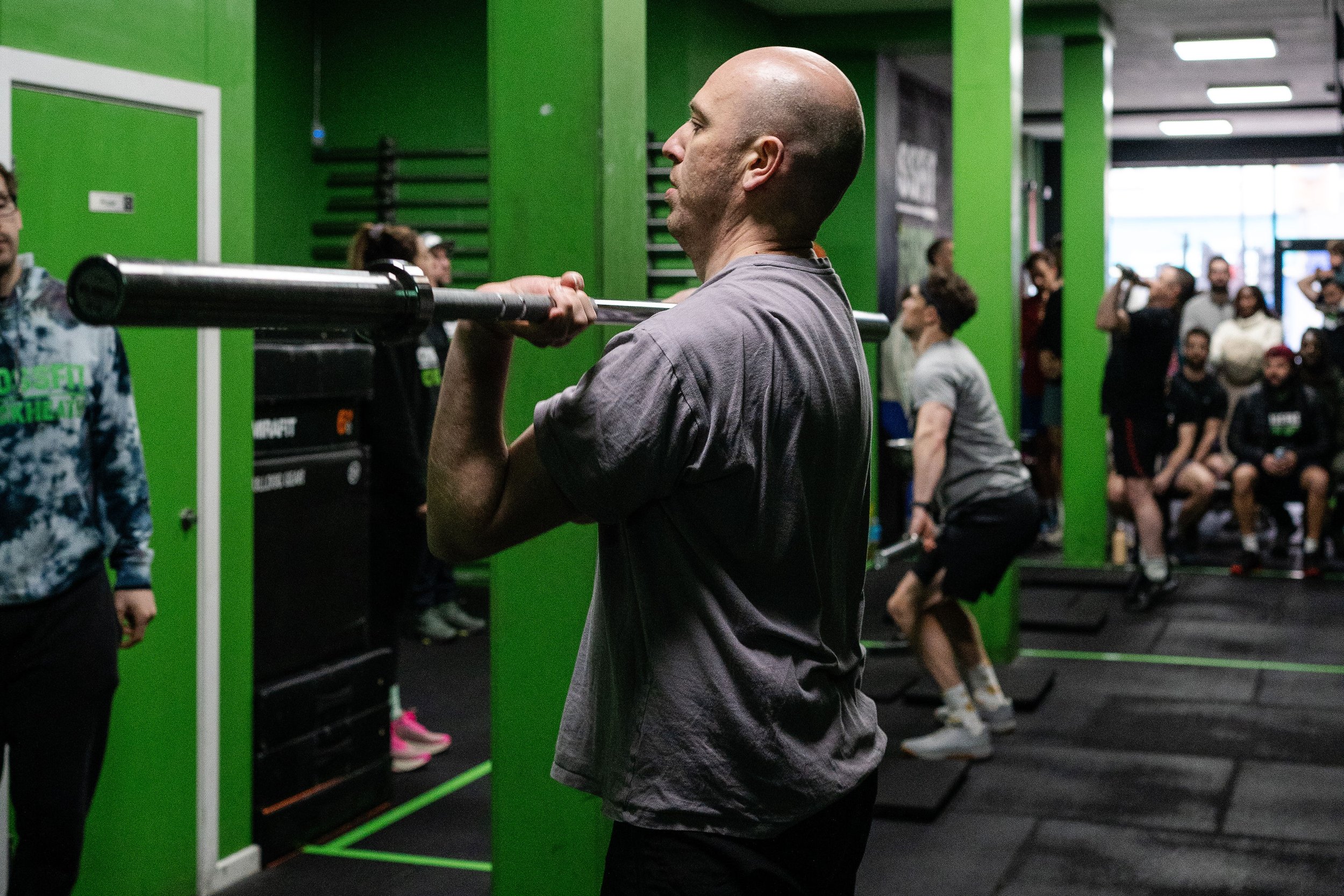 Man lifting a barbell in a gym with people in the background