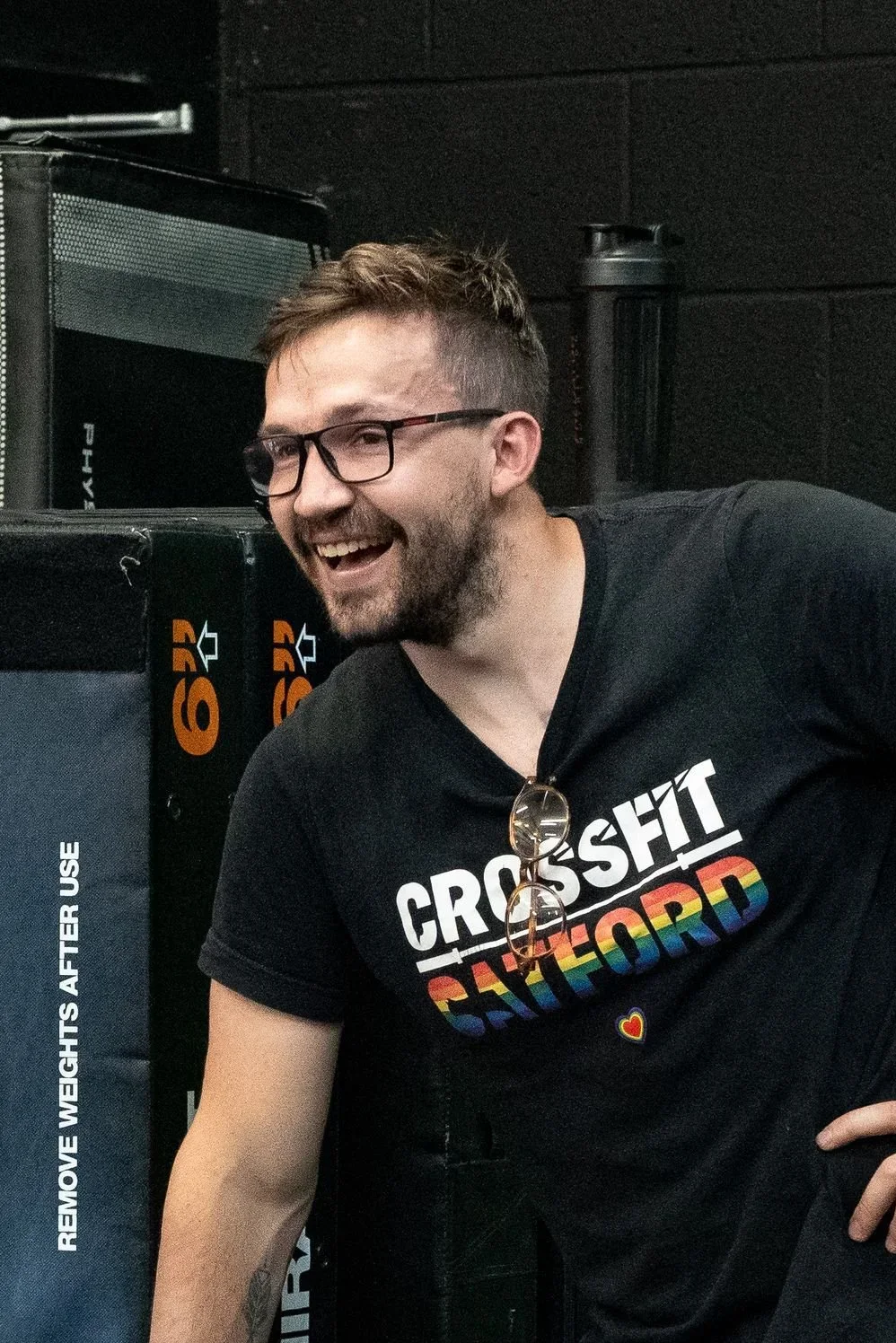 Person smiling with glasses wearing a black sweatshirt against a black background.