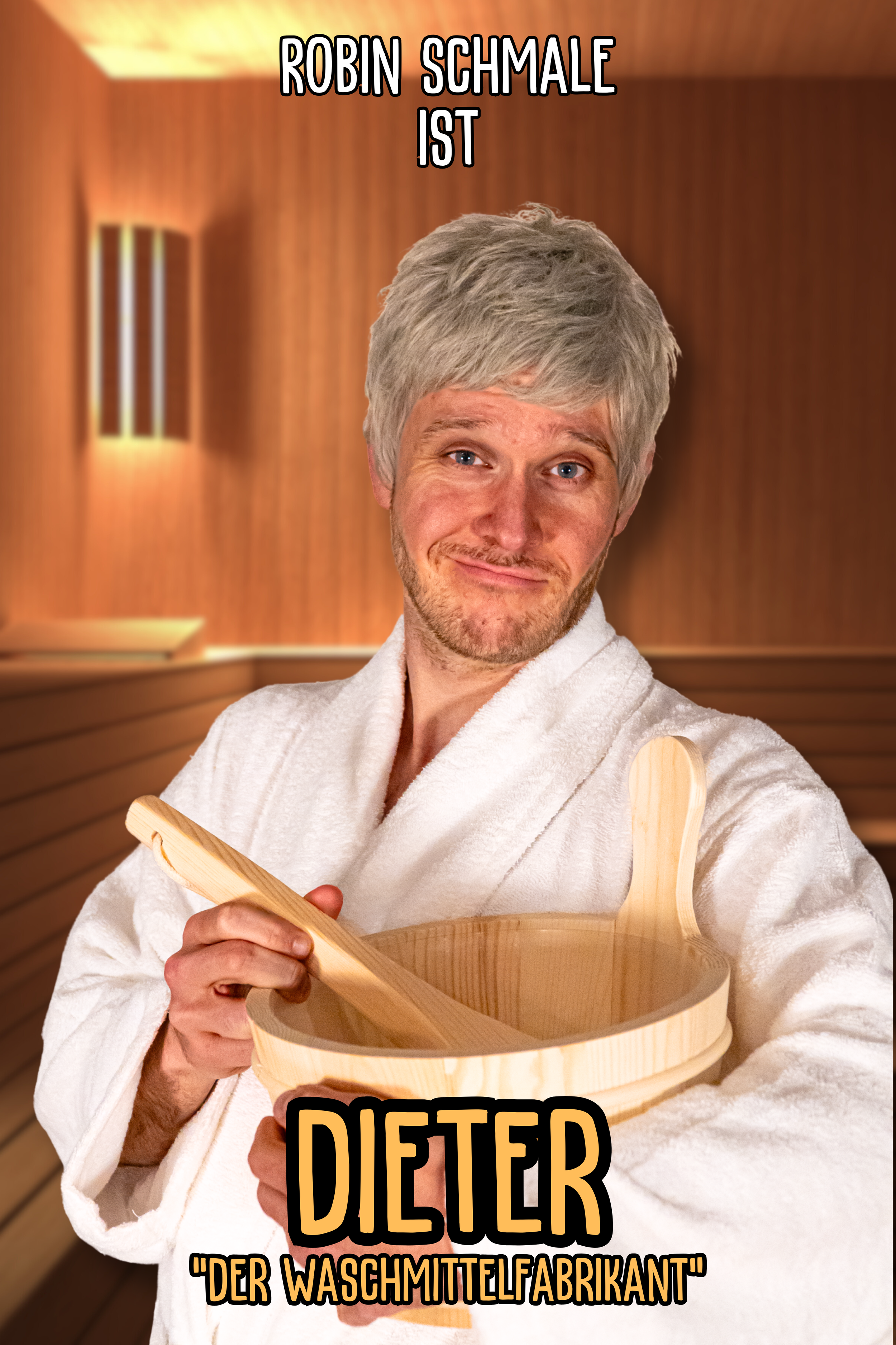 Ein Mann mit grauem Haar und Bart trägt einen weißen Bademantel, hält einen Holzkochlöffel und eine Holzpfanne, steht in einer warm beleuchteten Sauna oder Spa. Der Text auf dem Bild lautet: "Robin Schmale ist Dieter, der Waschmittelfabrikant".