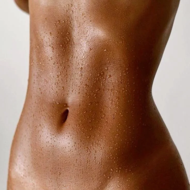Close-up of a woman's midsection, showing the stomach and waist with water droplets on the skin.