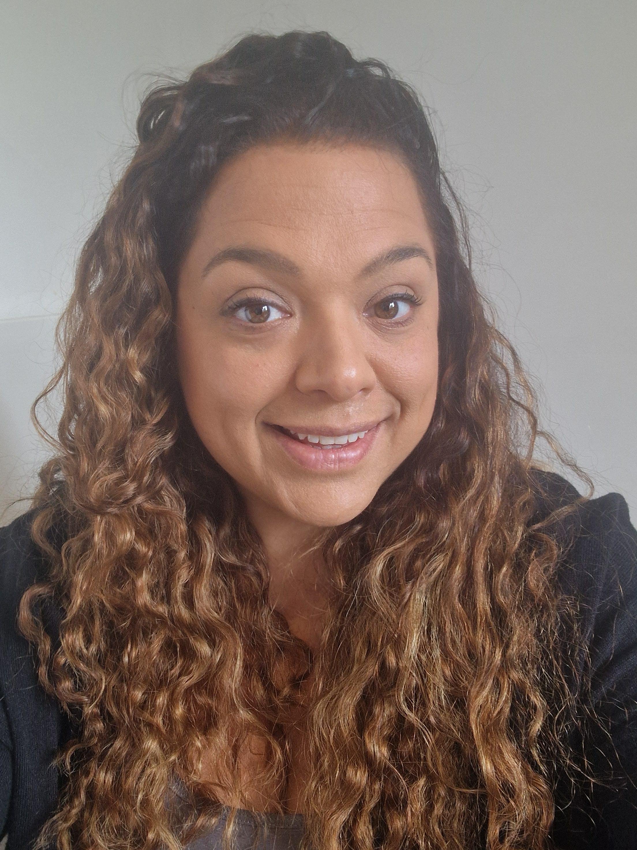 Close-up of Lisa Upshon, a smiling woman with long, curly brown hair and brown eyes, wearing a black top, facing the camera against a plain background.
