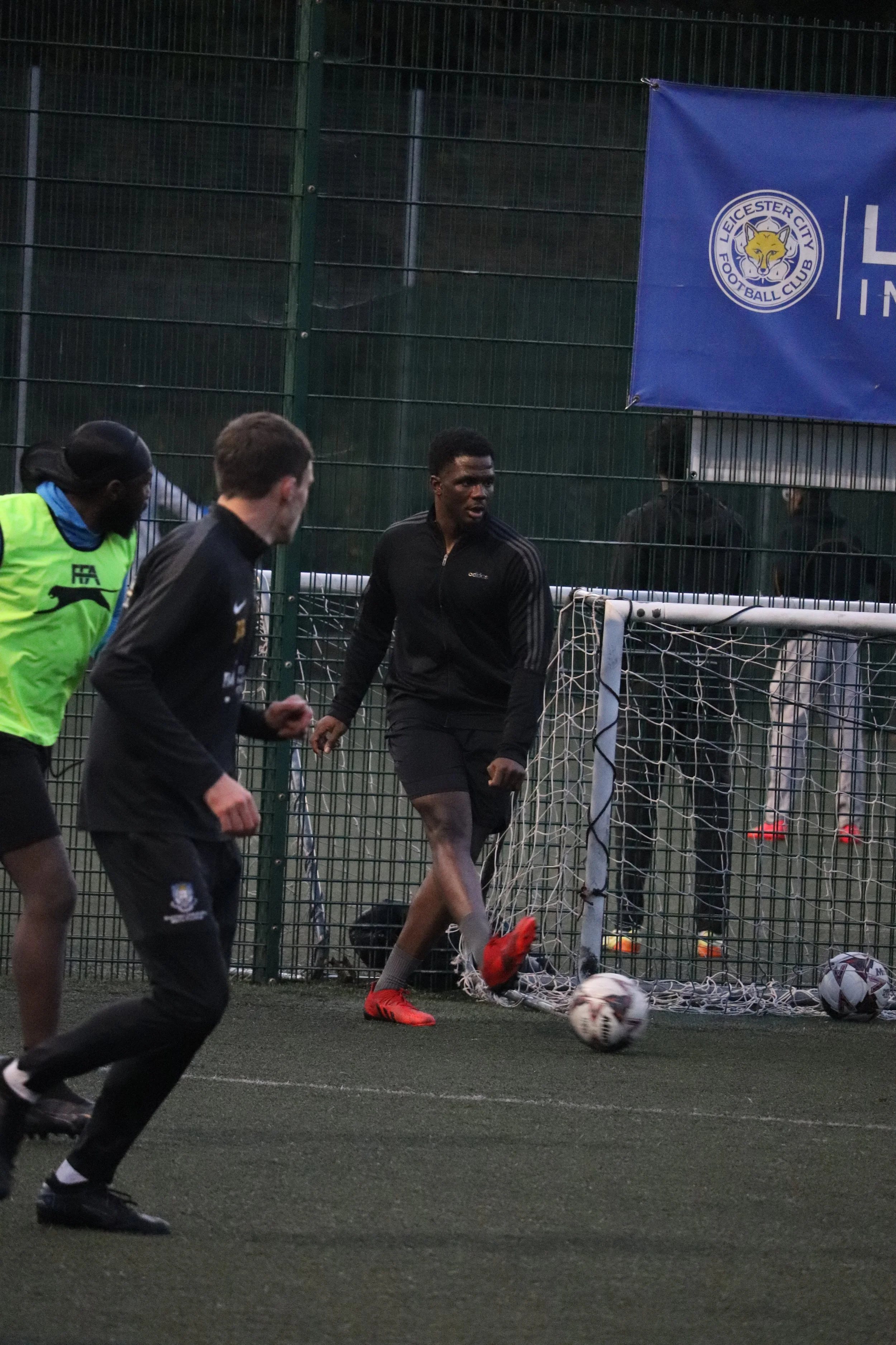 Soccer players during a practice session on an outdoor field with a Leicester City Football Club banner.