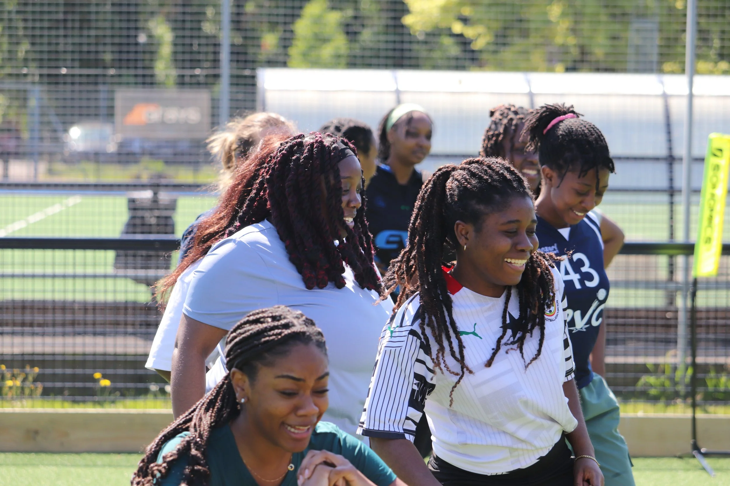 Group of women football players with dreadlocks smiling after a game on an outdoor field.