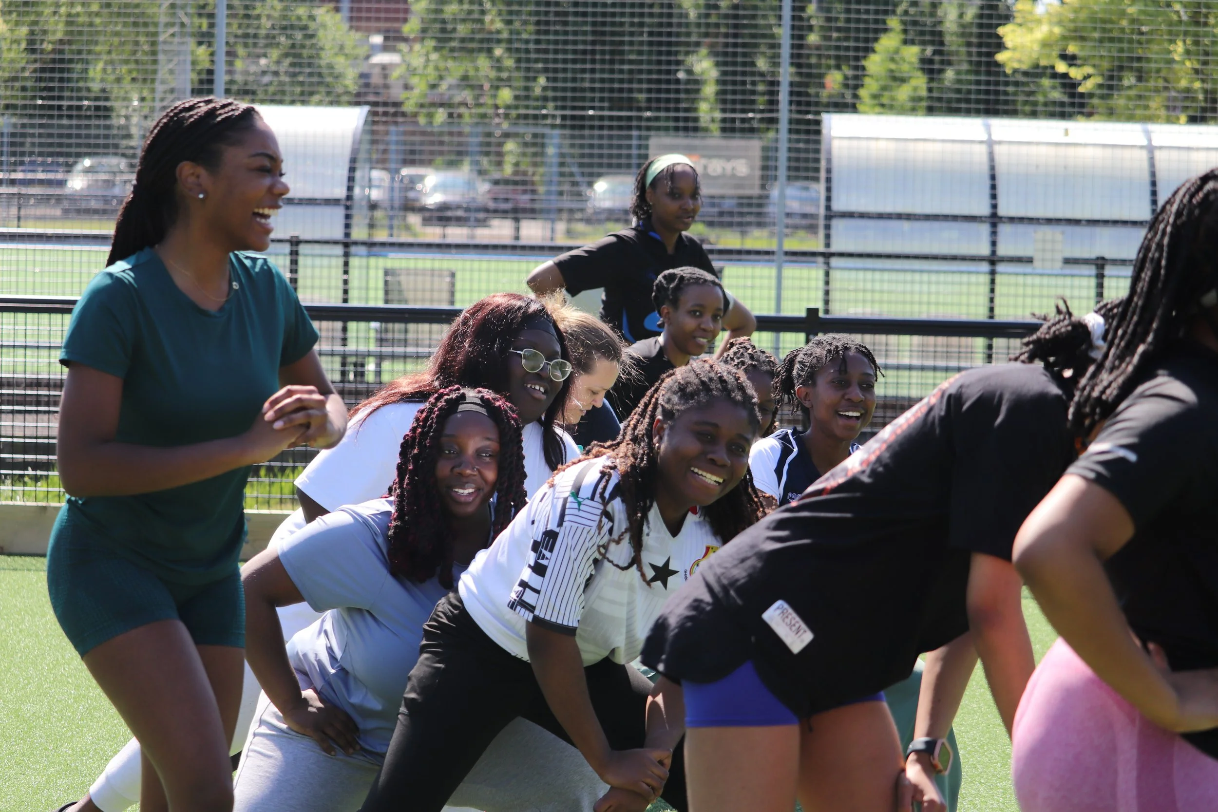 Women and girls participating in a tug-of-war game on a sports field, smiling and having fun.