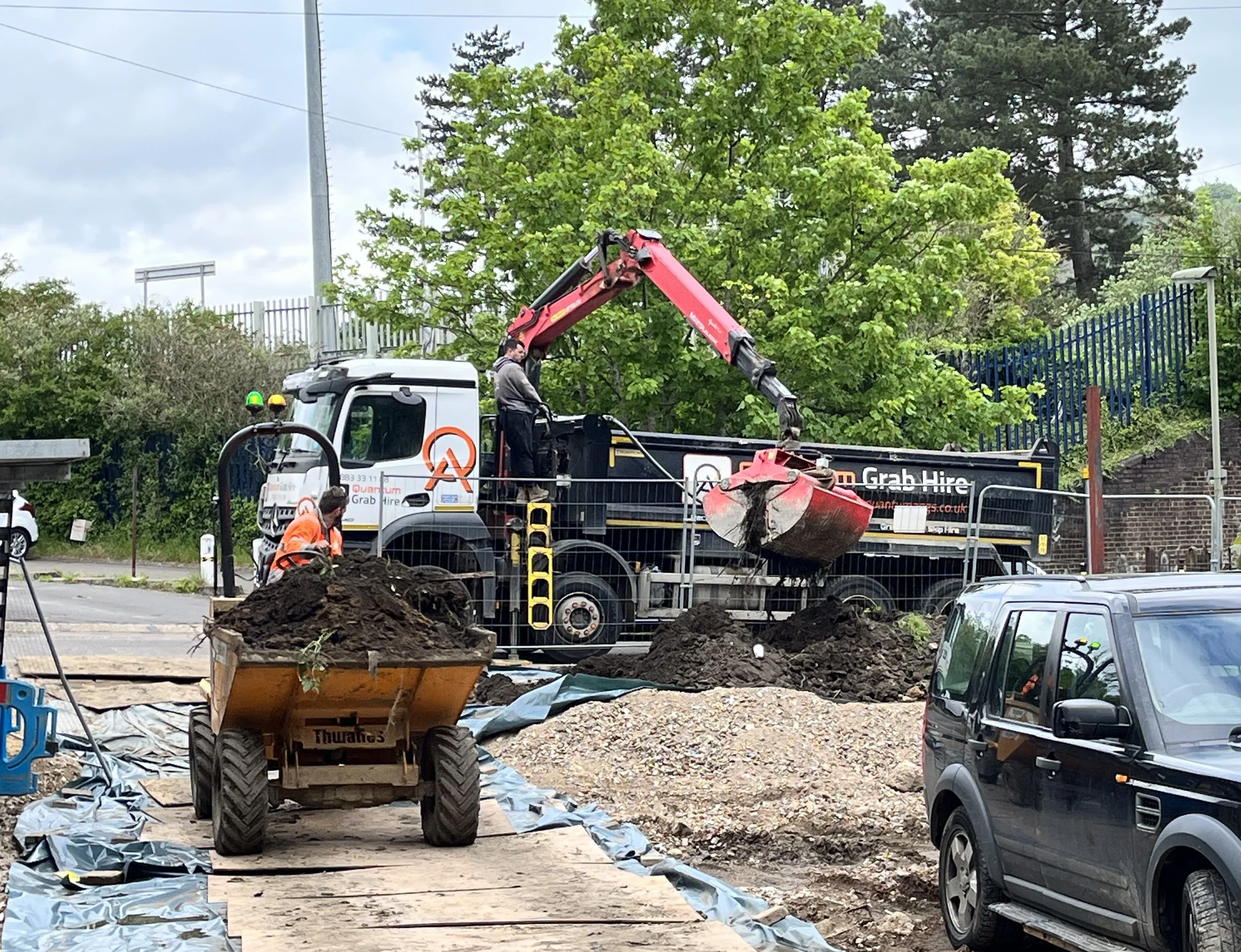 Construction workers working at a site with a large grab truck and piles of dirt and gravel.