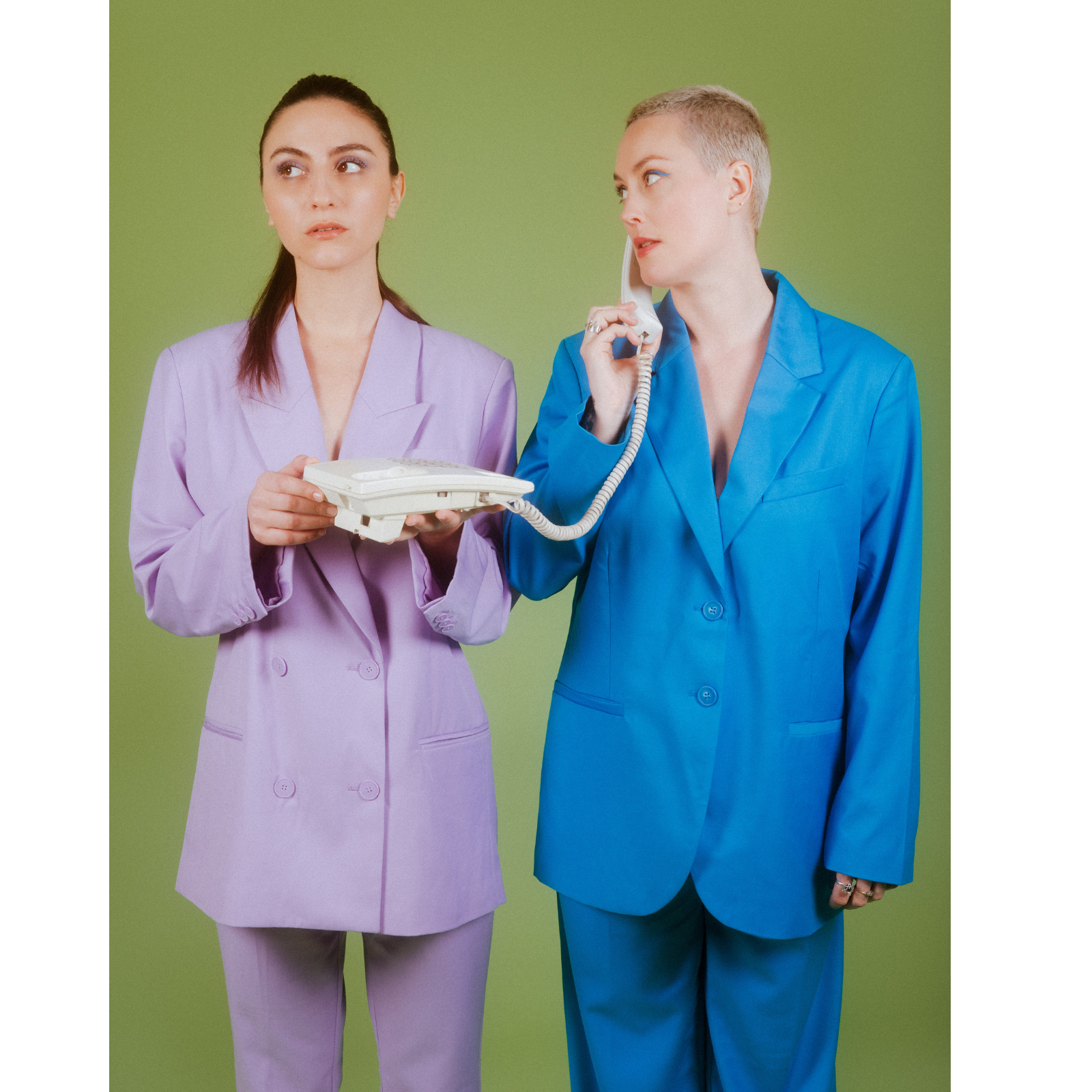Two women in pastel-colored suits, one in lavender holding a landline phone and the other in bright blue talking on the phone against a green background.