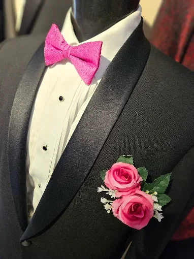 Black tuxedo with satin lapel, white dress shirt, pink bow tie, pink roses boutonniere on the lapel.