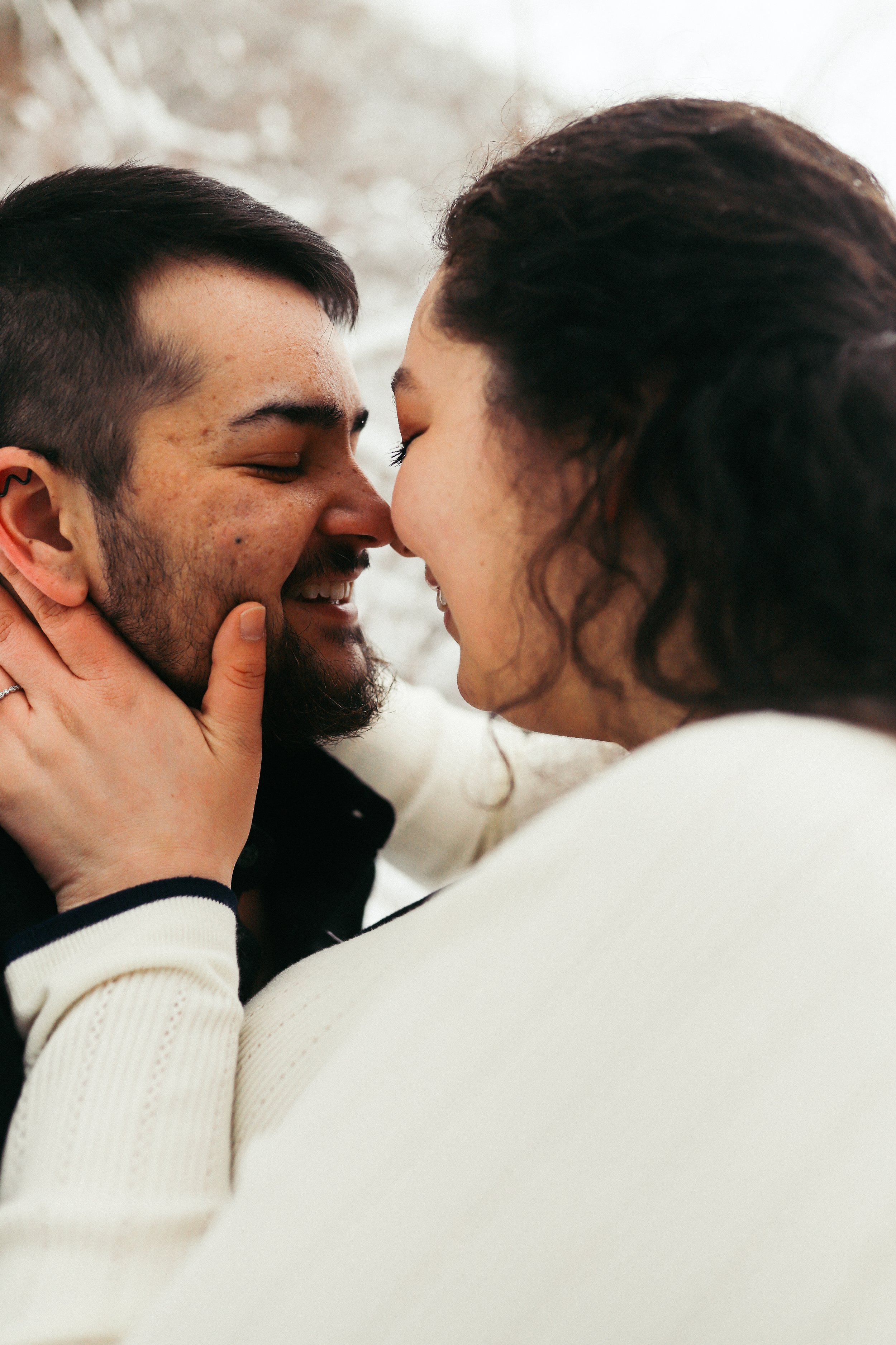 A couple touching noses and holding each other's faces, smiling warmly at each other.
