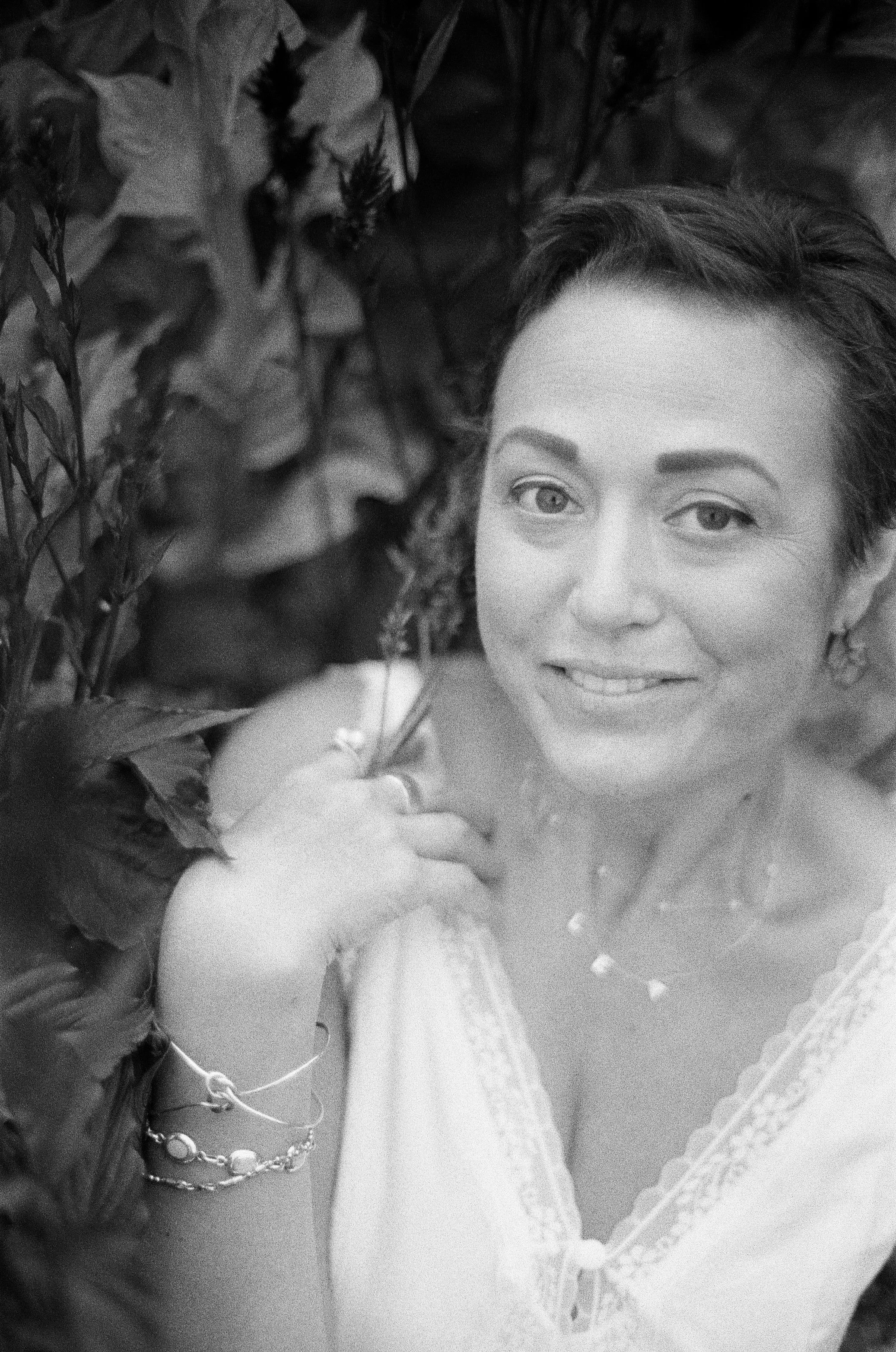 A woman with short hair smiling at the camera surrounded by greenery.