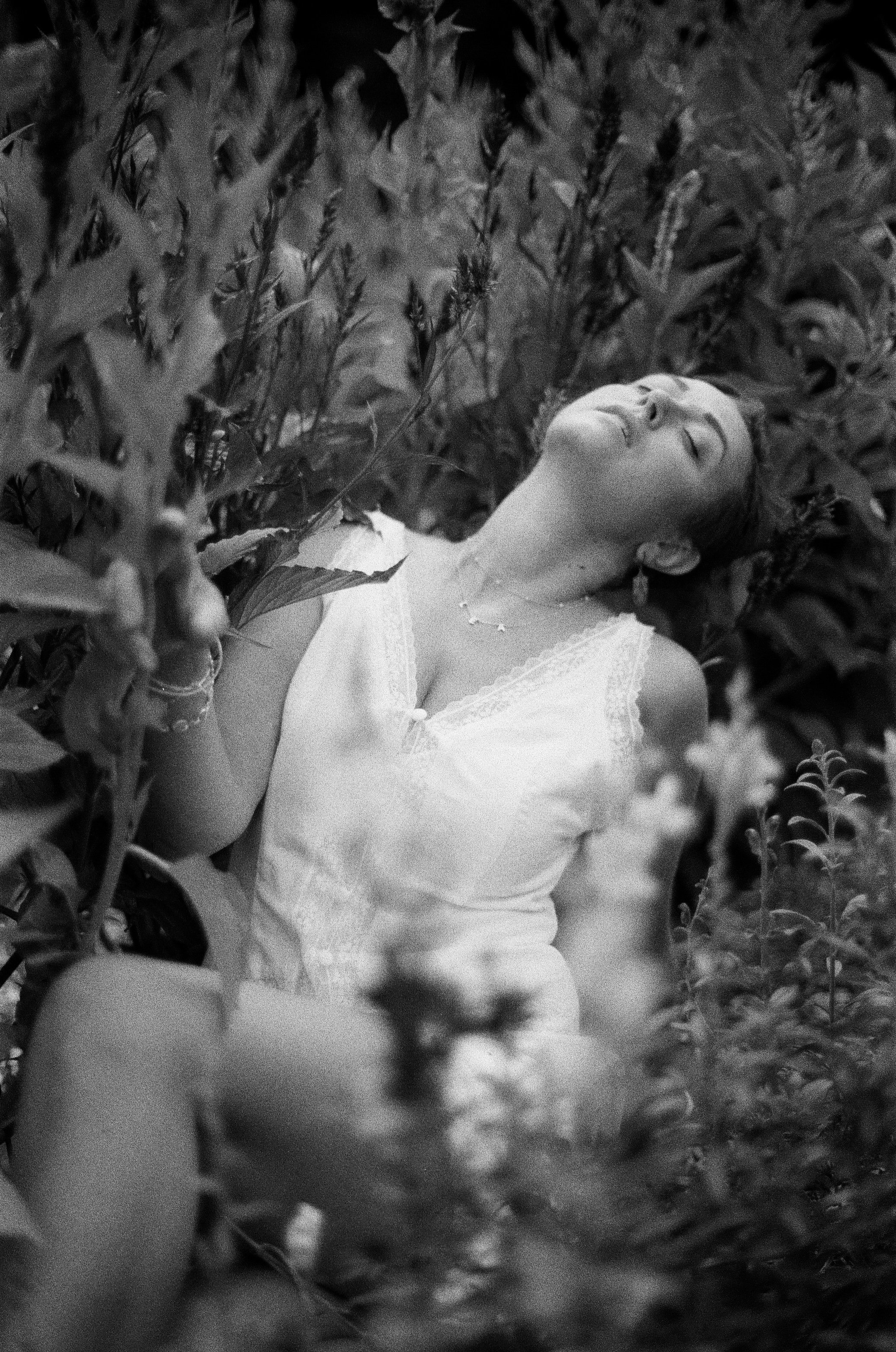 A woman in a white dress lying amidst tall grasses in a field with her eyes closed