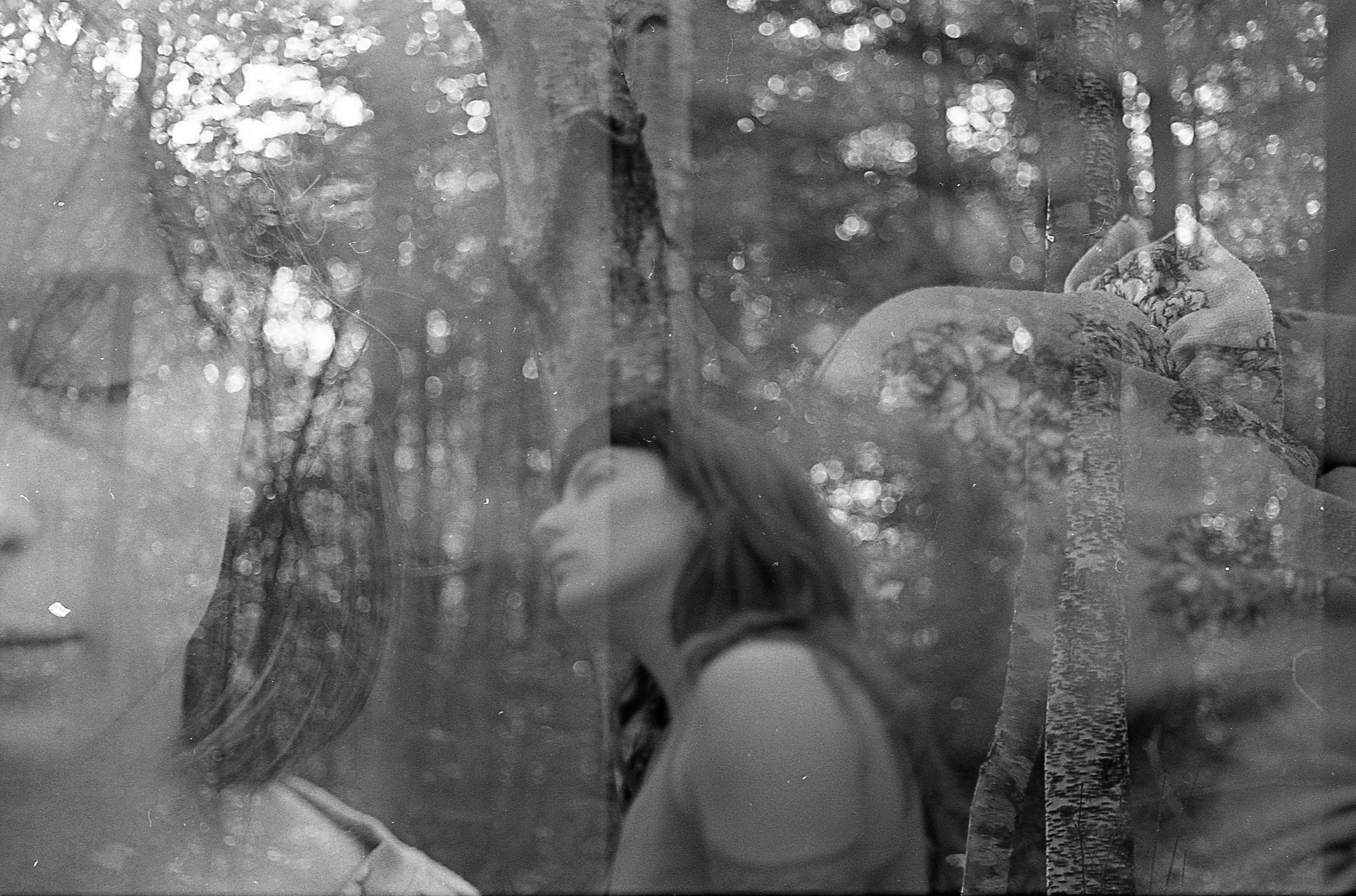 A double exposure black and white photo combining a close-up of a woman's face and a scene of women sitting outdoors in a wooded area.
