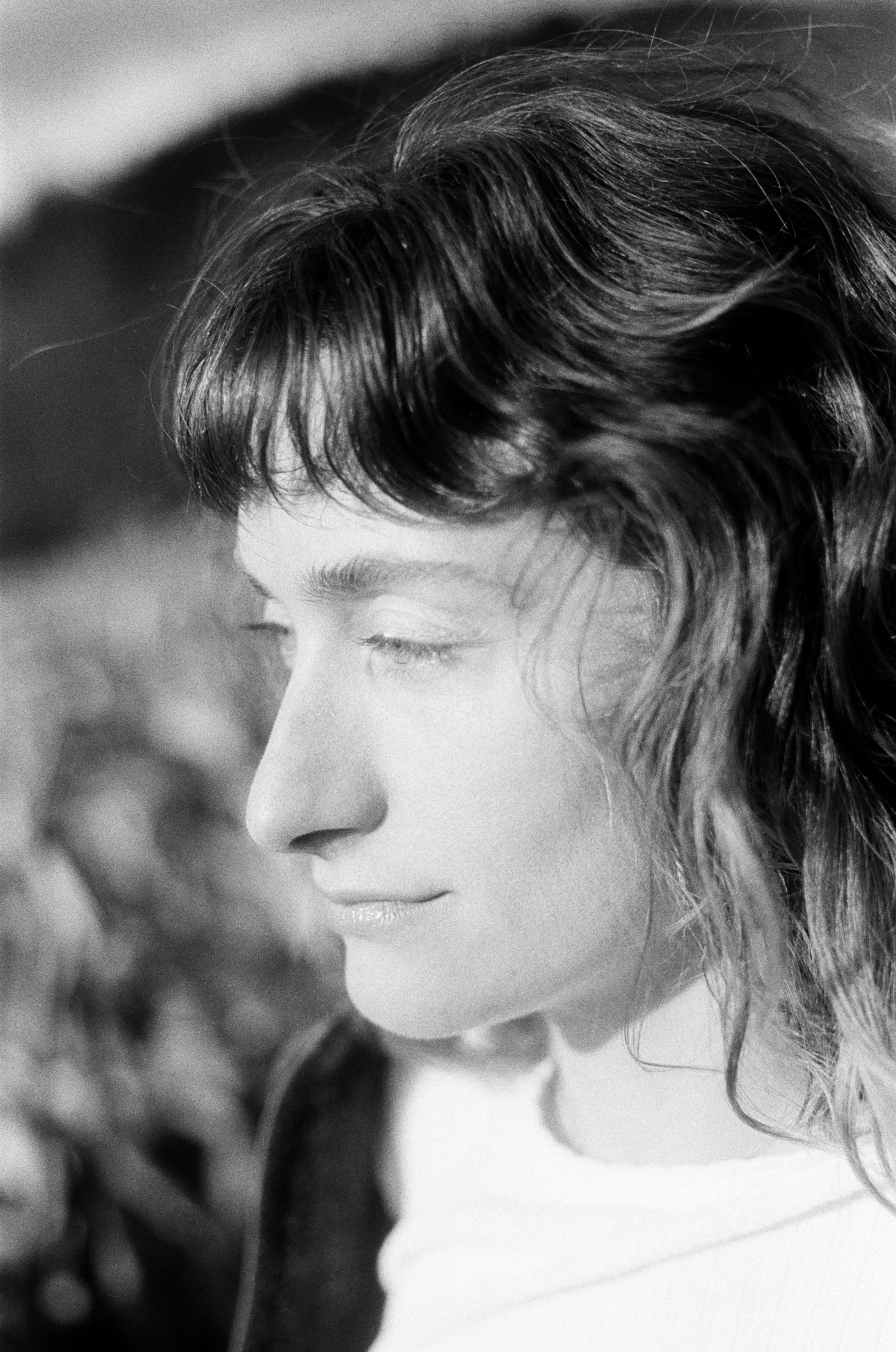 Black and white close-up portrait of a woman with closed eyes and wavy hair, smiling softly.