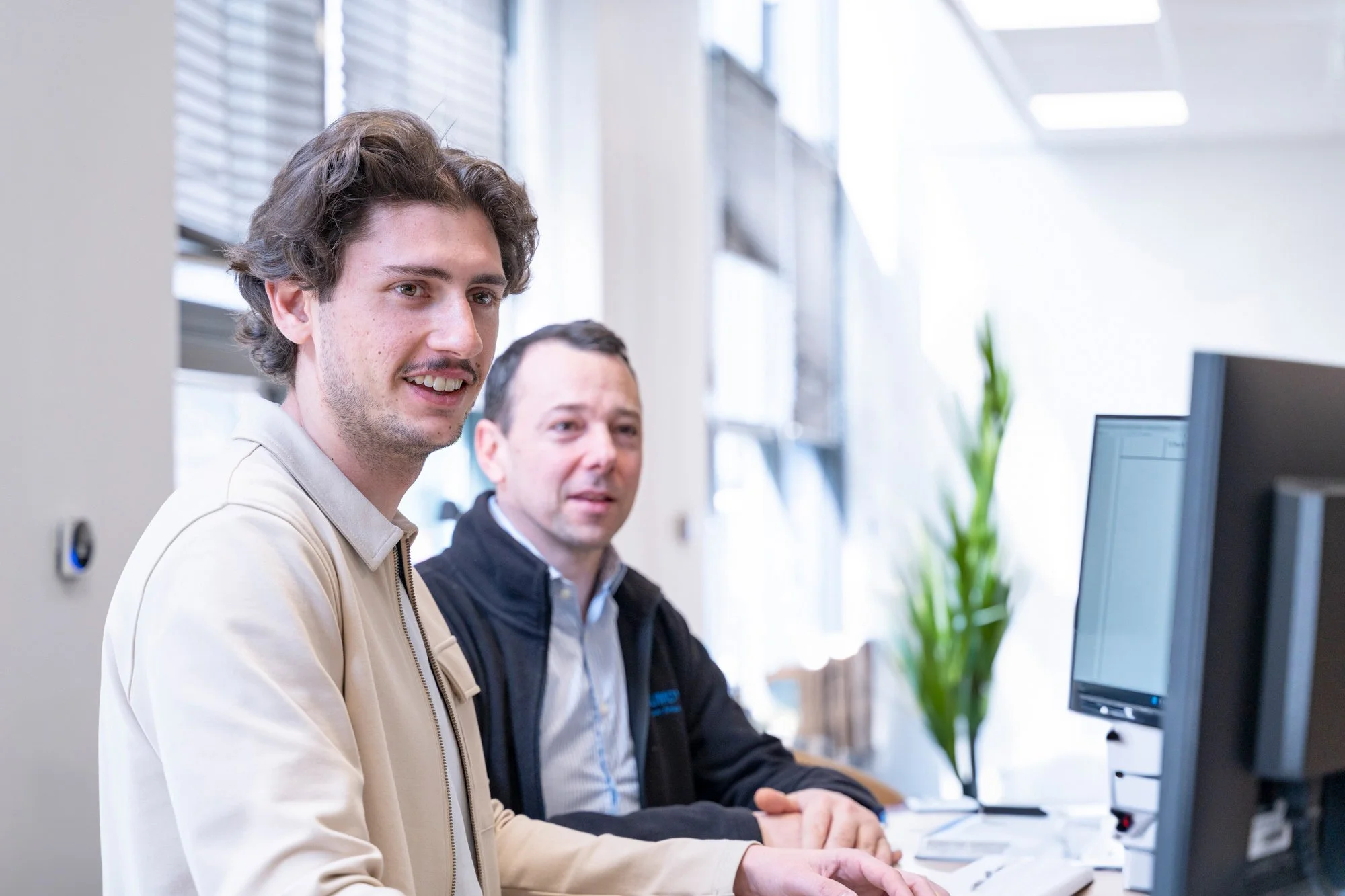 Jules Boschard du graduate programe Batibig et un dirigeant du groupe travaillent sur un ordinateur dans un bureau lumineux.