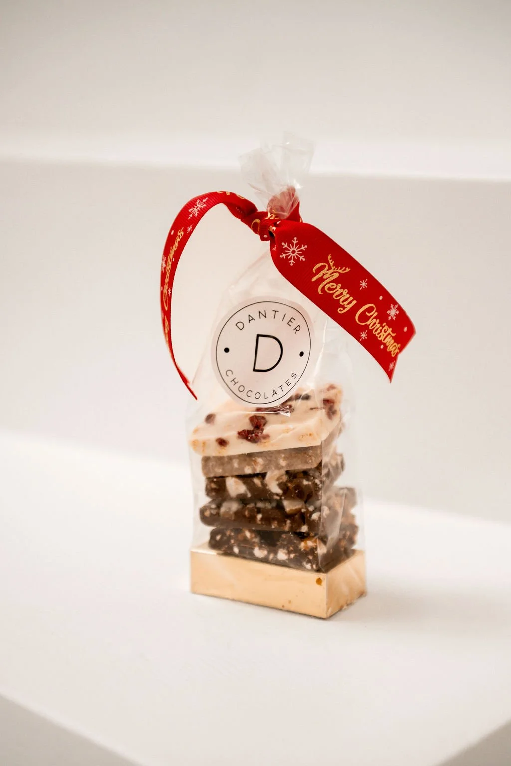 Zak met chocolade, versierd met een rood lint en "Merry Christmas" tekst, merknaam "Dantier Chocolates."