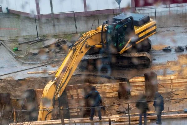 Heavy earthmoving machinery excavating ground on a rainy day with construction workers nearby