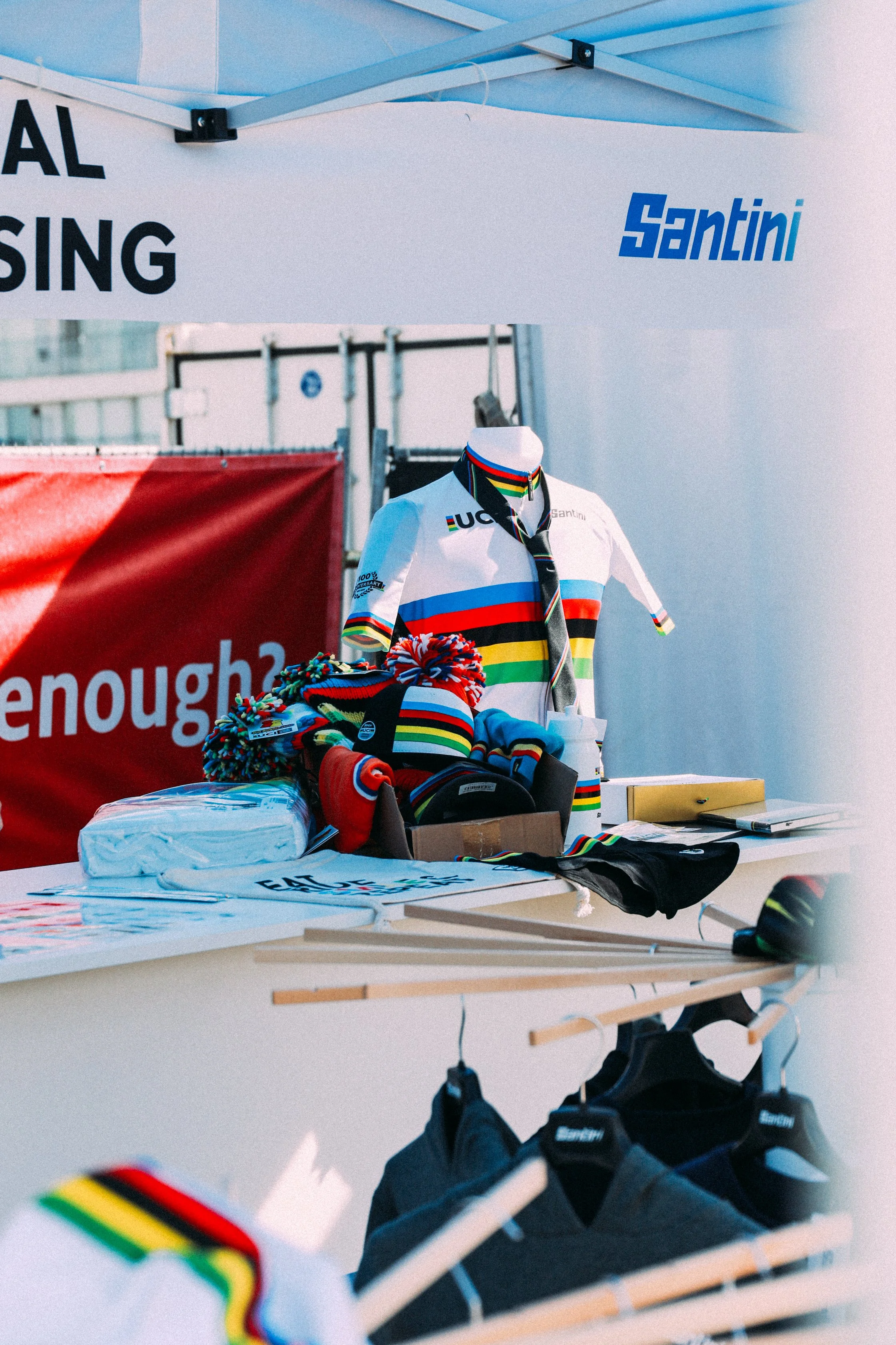 Cycling merchandise display at a booth with jerseys, hats, and accessories. "Santini" brand visible.